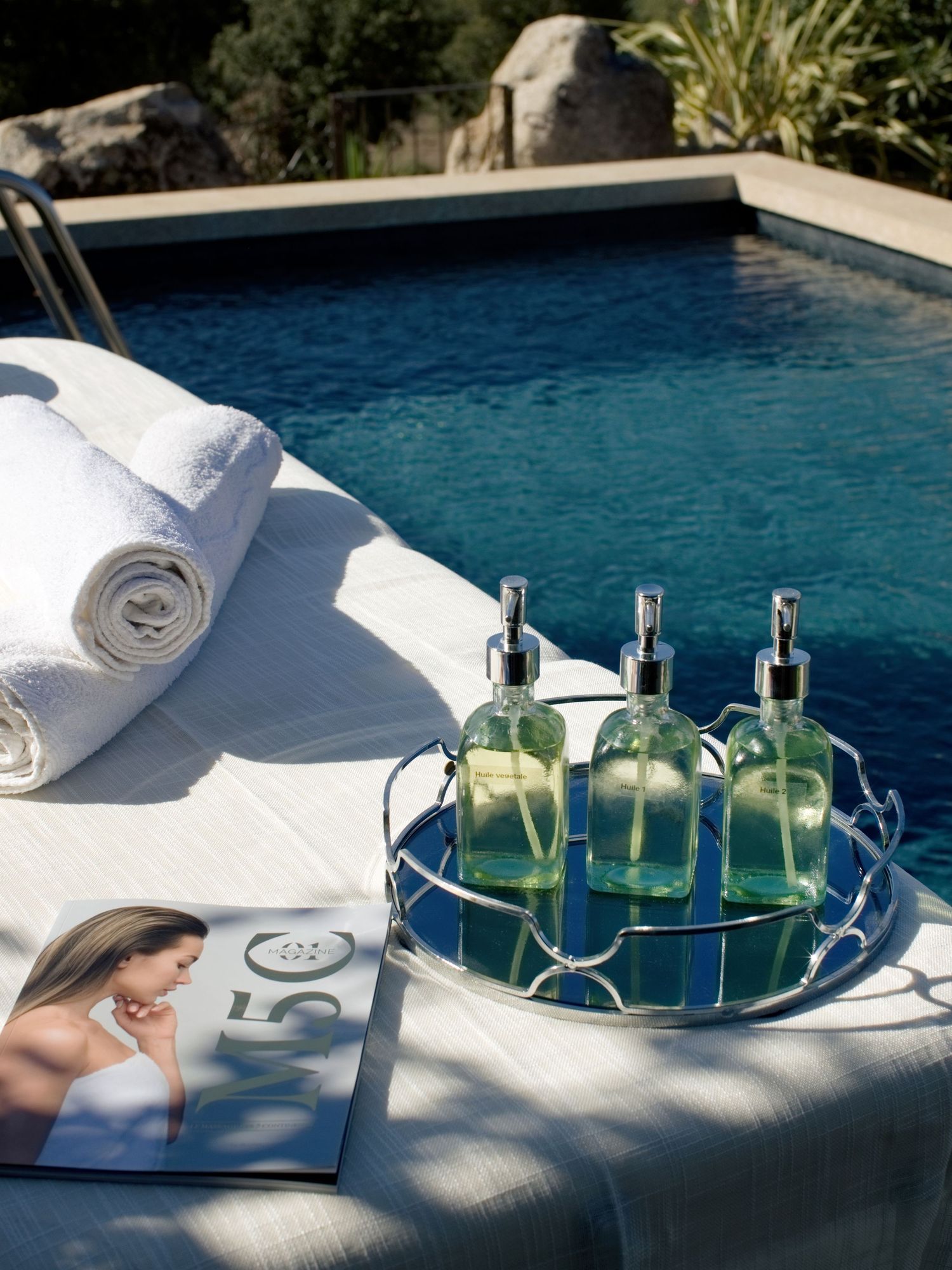 Aménagement de spa de luxe au bord de la piscine avec serviettes blanches roulées, distributeurs de lotion en verre vert sur plateau argenté