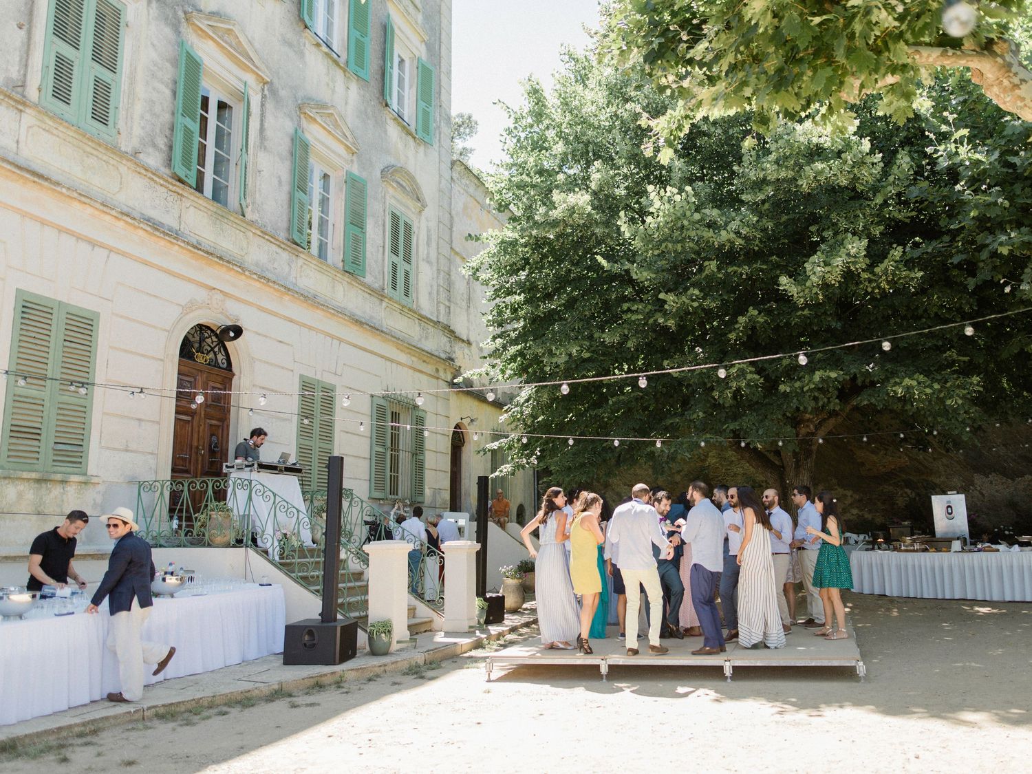 Elegant outdoor wedding reception at a French chateau with string lights, guests mingling on a dance floor surrounded by lush trees.