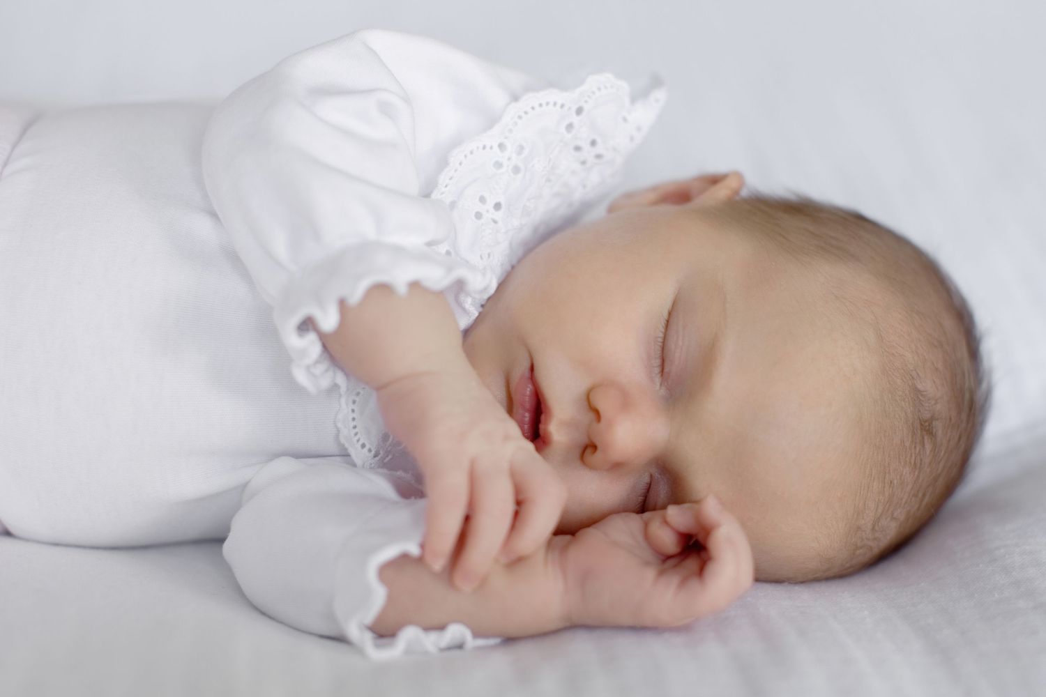 Un nouveau-né paisible dort en tenue blanche sur un fond blanc doux.