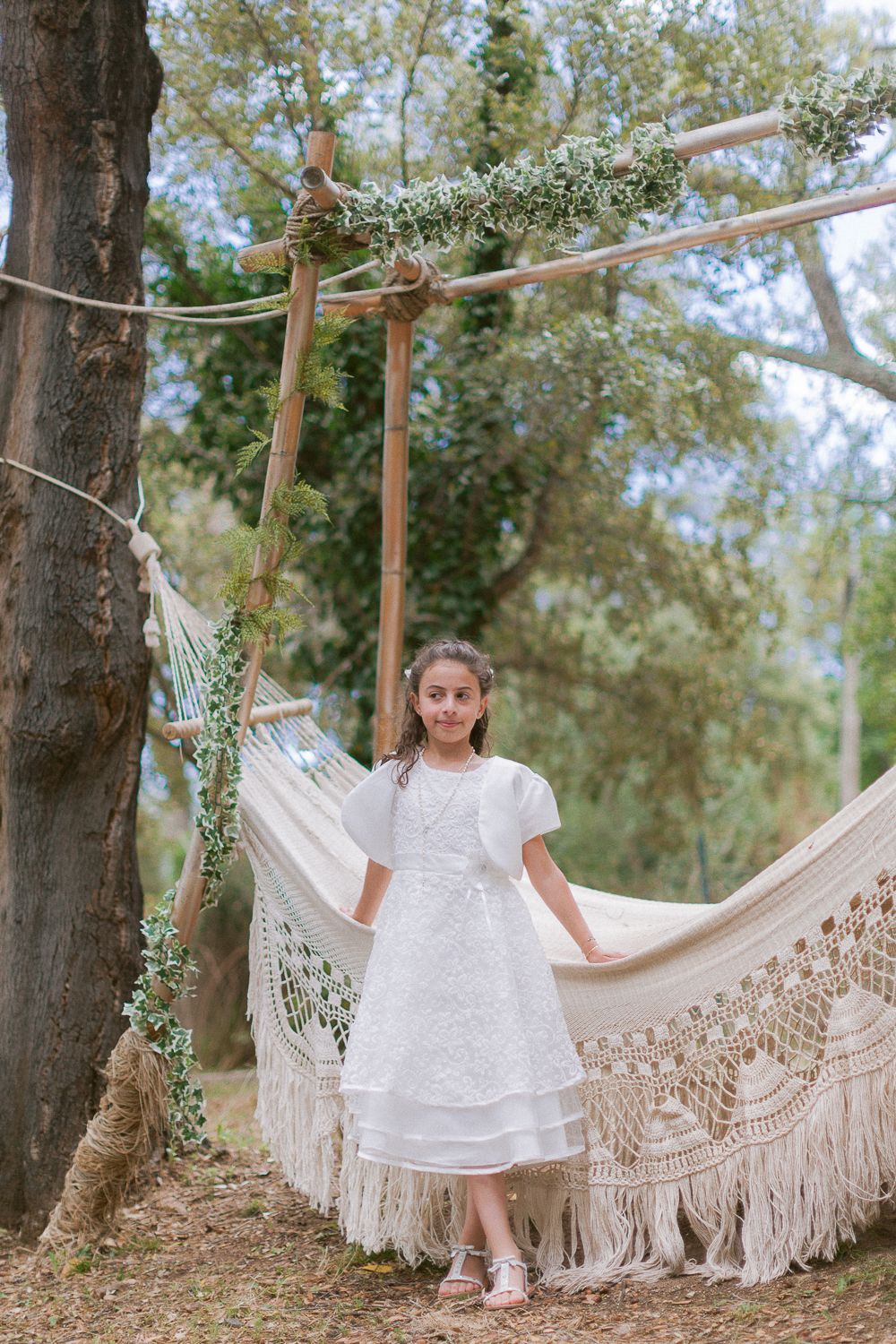 Jeune fille en robe de communion blanche, debout à côté d'un hamac en macramé en Corse.