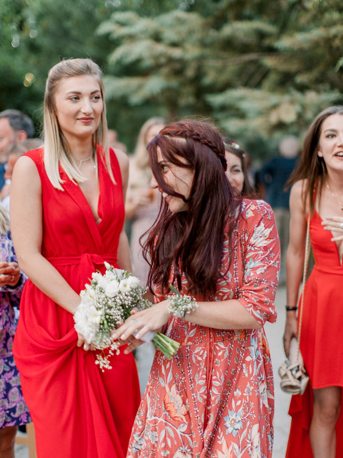 Des femmes en robes rouges assistent à un mariage, l'une d'elles tenant un bouquet blanc, souriant et discutant en plein air.