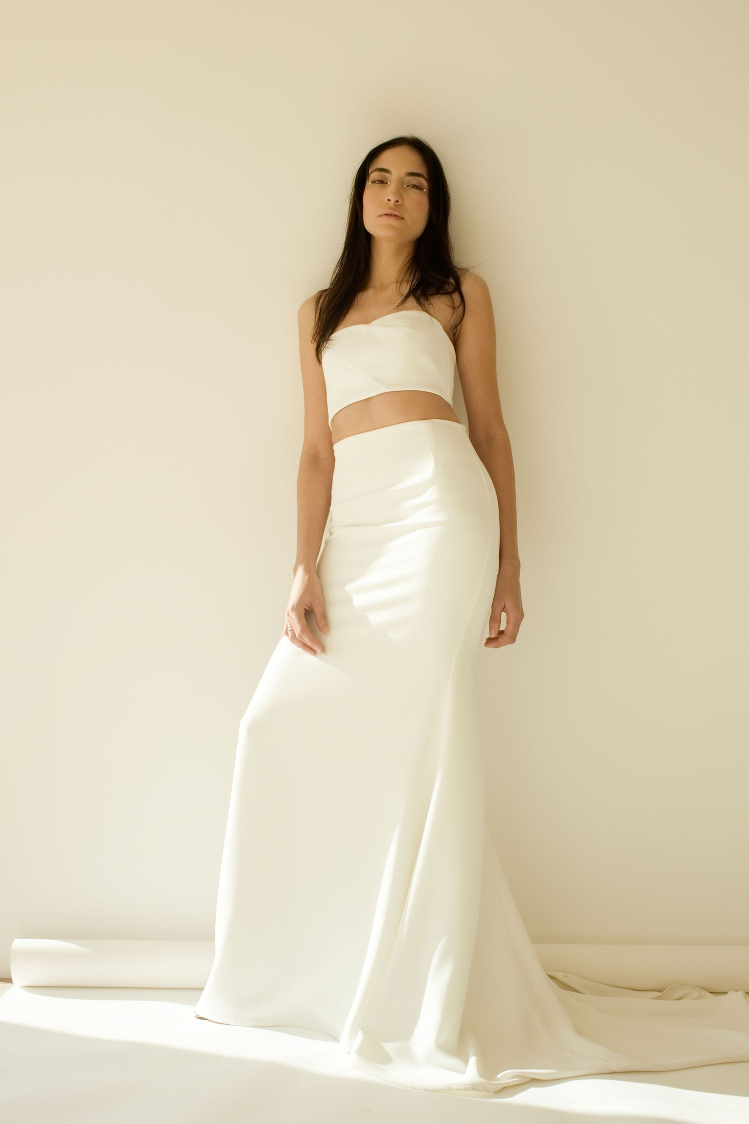 Mannequin portant un ensemble de mariée deux pièces blanc composé d'un crop top bustier et d'une jupe longue en satin avec traîne by romance