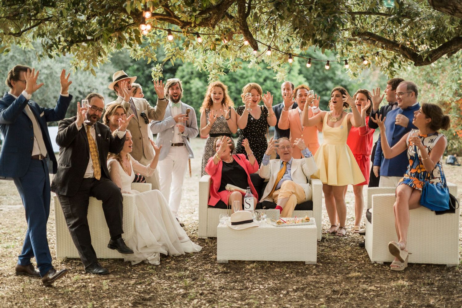 Photo de groupe joyeuse d'un cortège de mariage célébrant en extérieur sous des arbres illuminés de guirlandes lumineuses festives campomoro