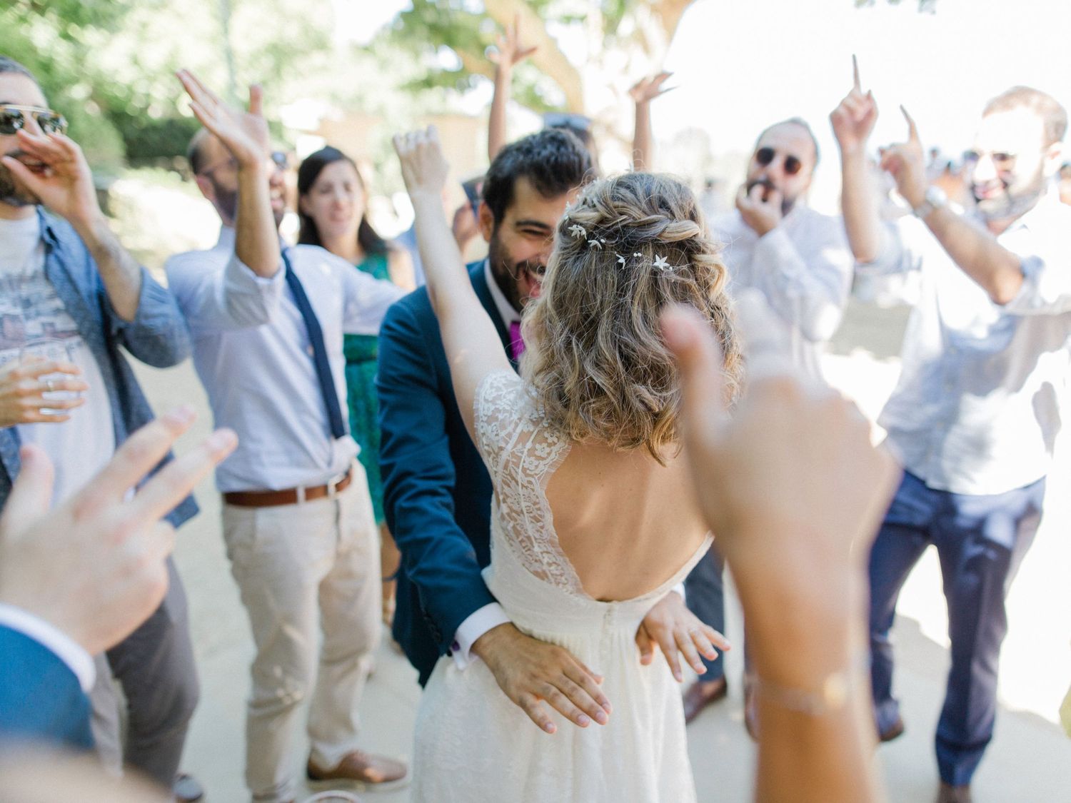 A joyful bride and groom embrace surrounded by cheering wedding guests outdoors in a candid celebration moment.