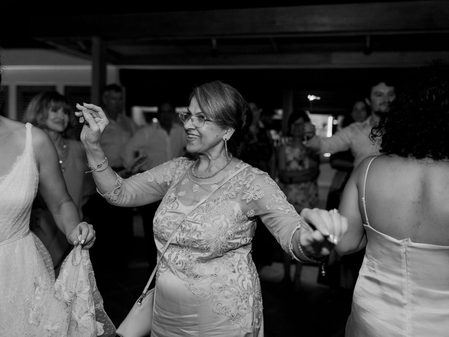 Photo en noir et blanc d'une femme en robe de dentelle dansant joyeusement lors d'une réception de mariage.