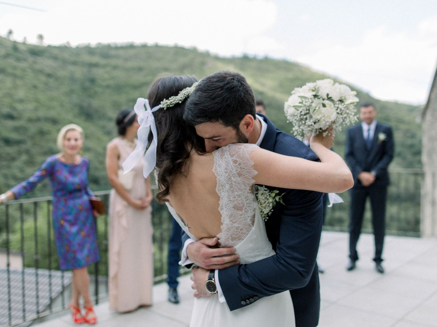 Bride and groom share emotional first look hug at outdoor wedding venue with lush green hills backdrop.