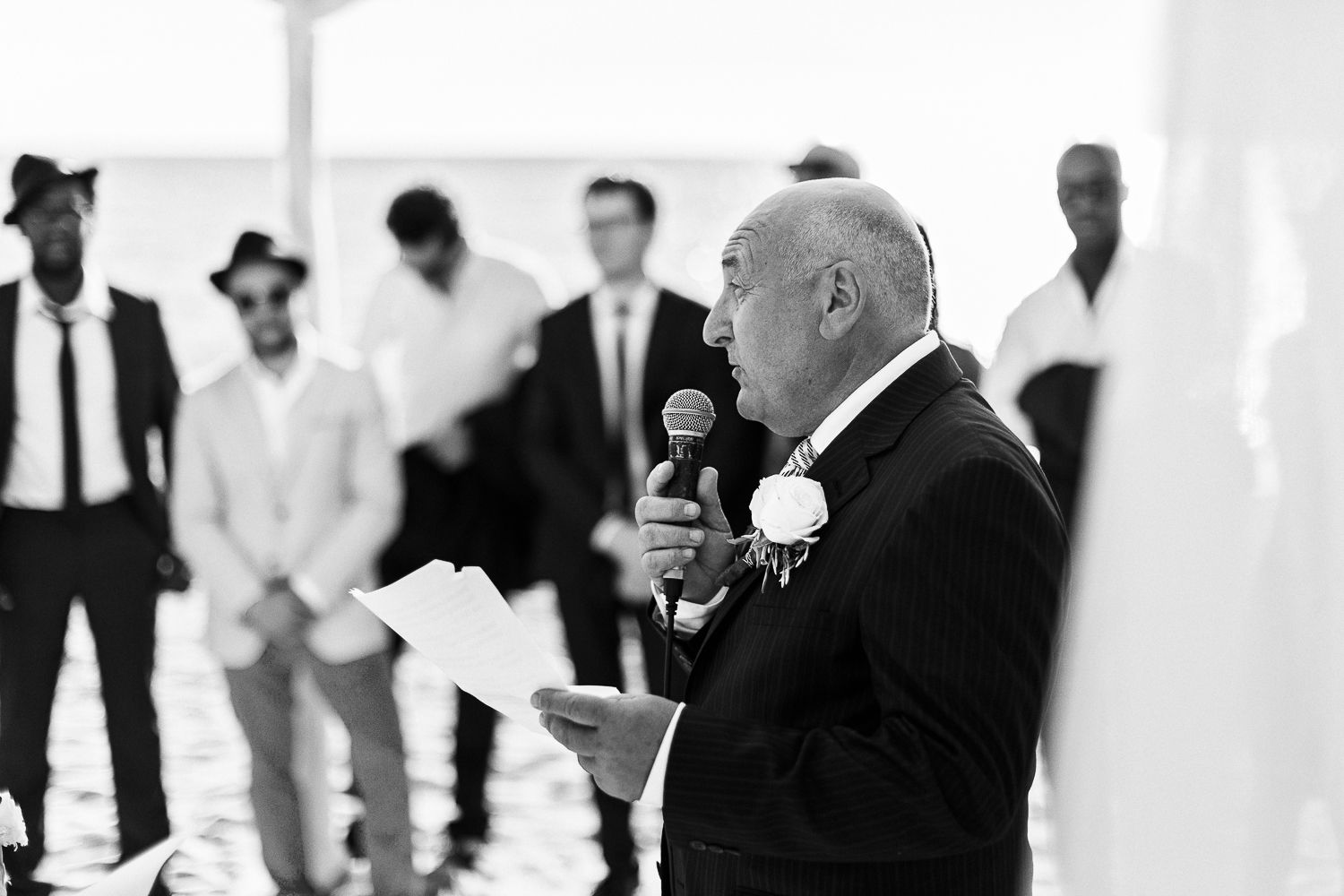 Un homme en smoking prend la parole lors d'une cérémonie de mariage, micro et feuille de papier à la main.