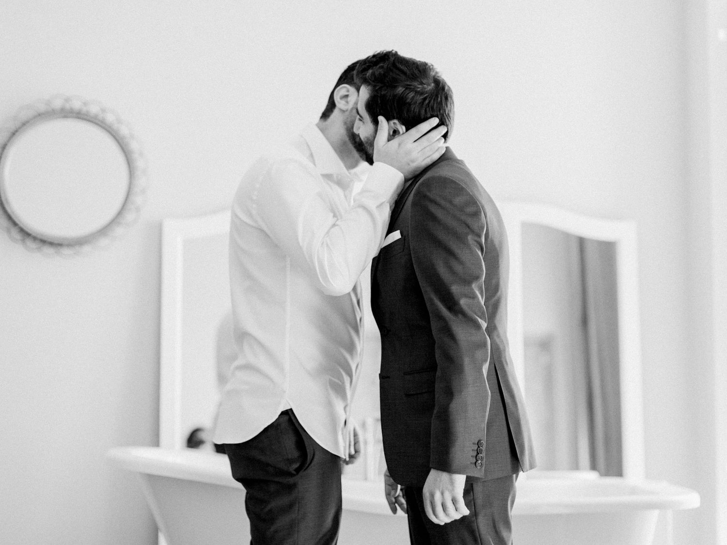 Black and white photo of two grooms sharing a tender kiss on their wedding day in an elegant room.