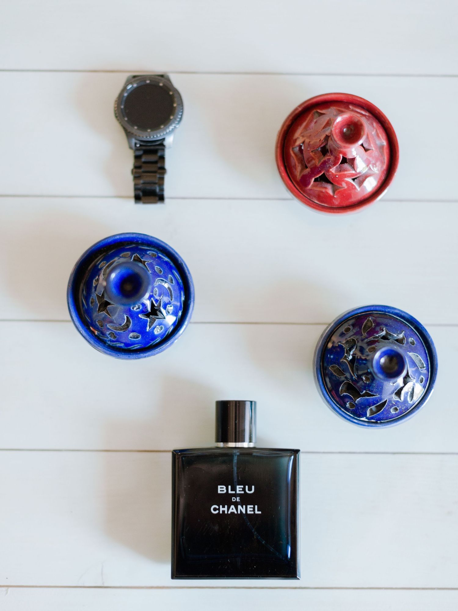 Flacon d'eau de toilette Bleu de Chanel présenté avec une montre connectée noire et trois coupelles décoratives colorées
