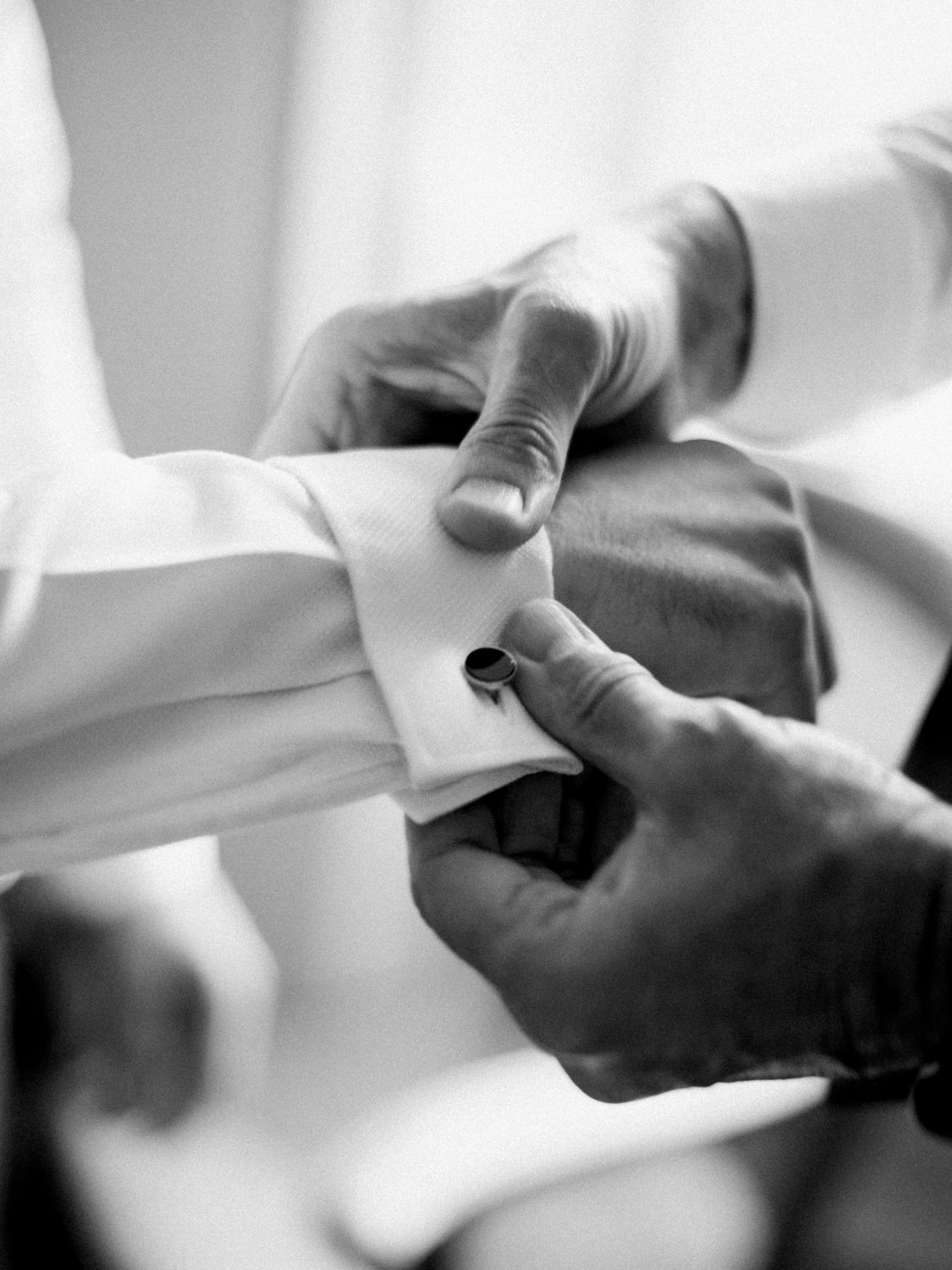 Black and white photo of a man fastening a cufflink on a white dress shirt sleeve.