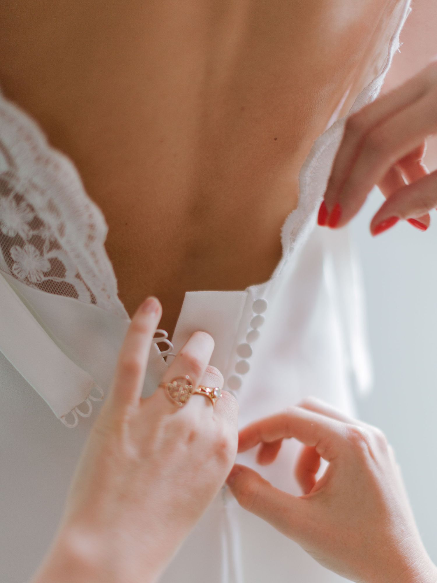 Gros plan sur des mains fermant de délicats boutons dans le dos d'une élégante robe de mariée en dentelle blanche.