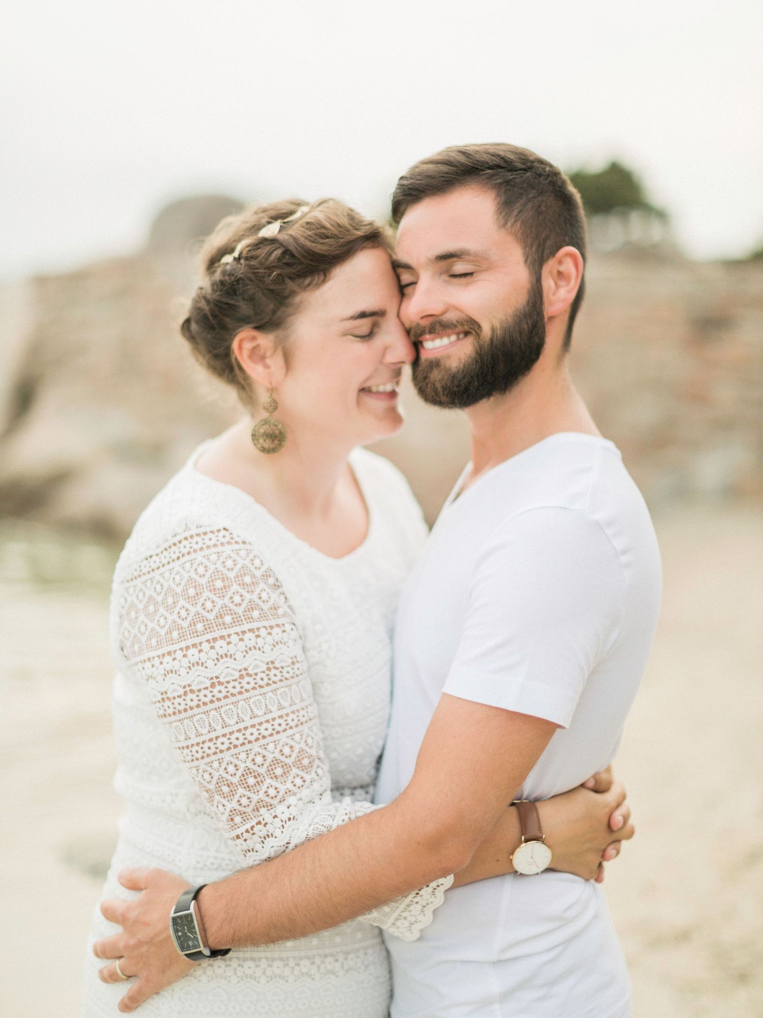 Un couple joyeux, les yeux fermés, partage un tendre moment sur une plage de sable fin baignée de soleil. Palombaggia Porto-Vecchio.