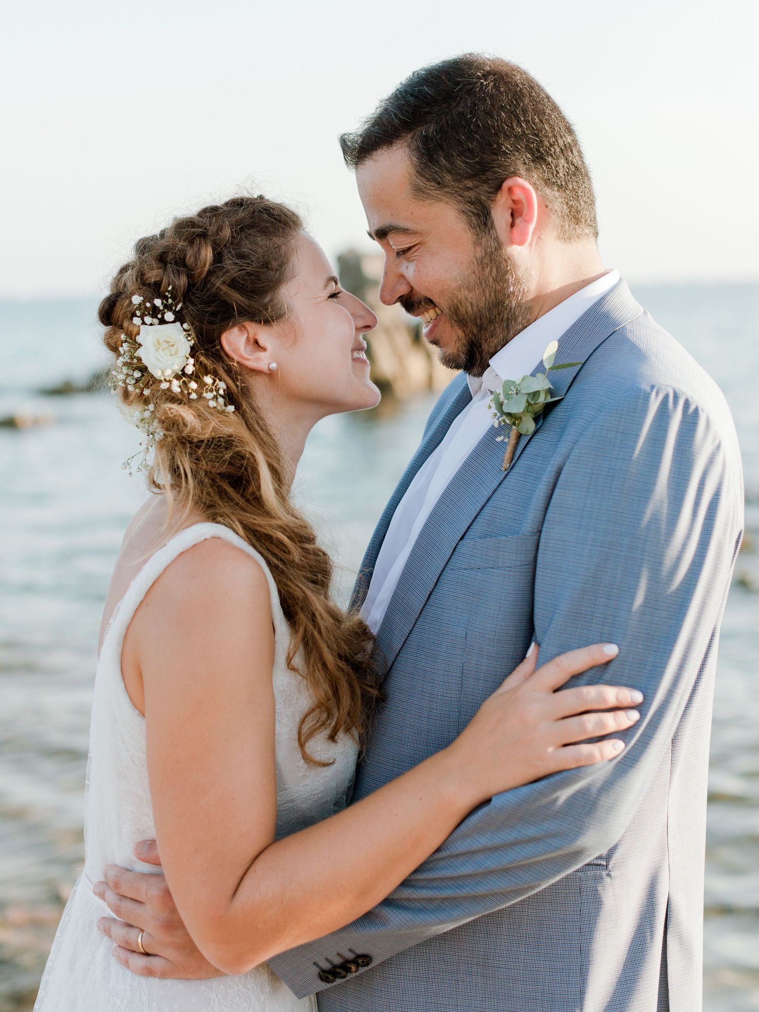 Les mariés partagent un moment intime au bord de l'océan, avec des accessoires de cheveux et une boutonnière fleuris.
