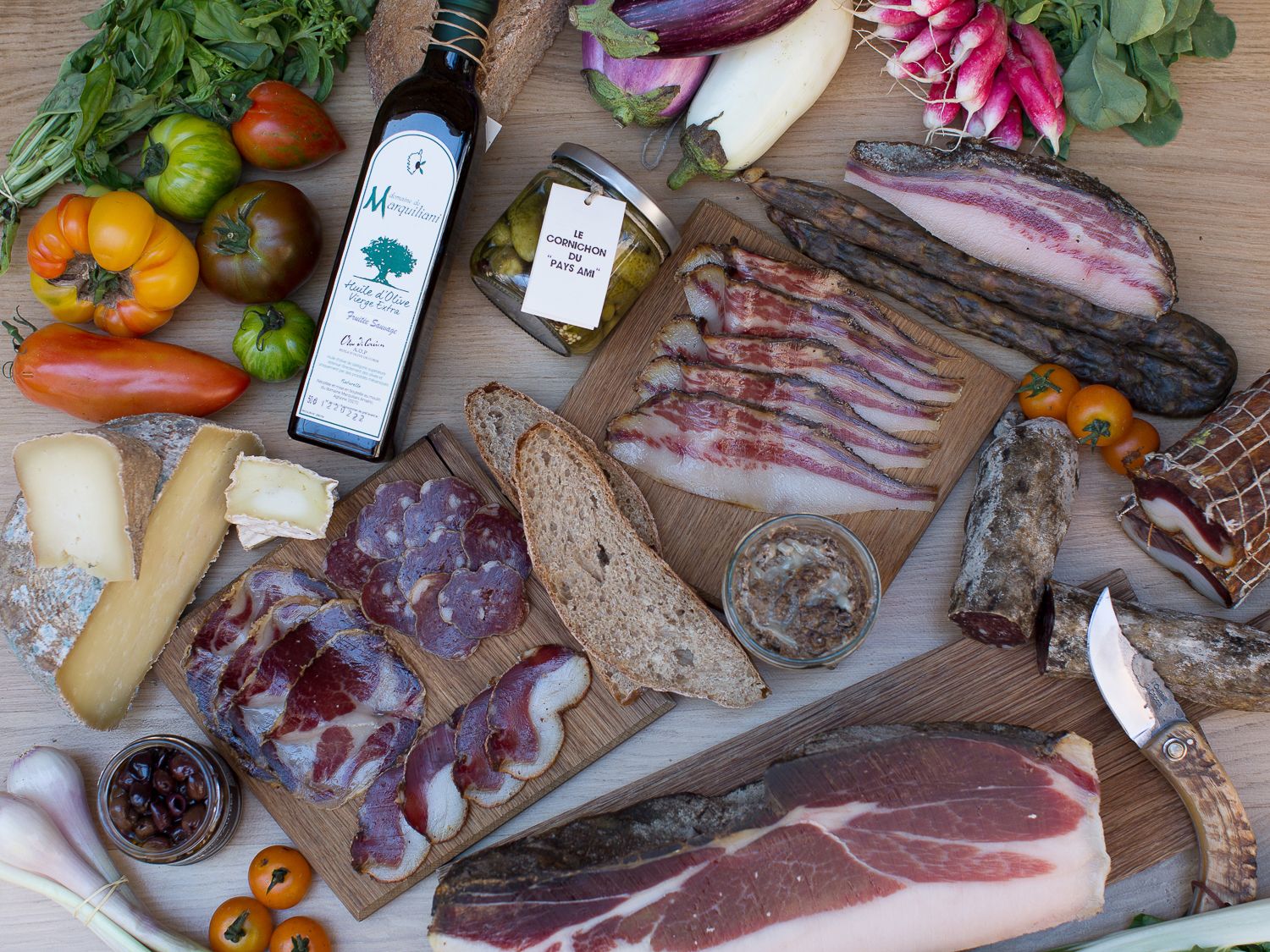 Plateau de charcuterie corse composé de viandes séchées, de fromages, de pain, d'huile d'olive et de légumes frais