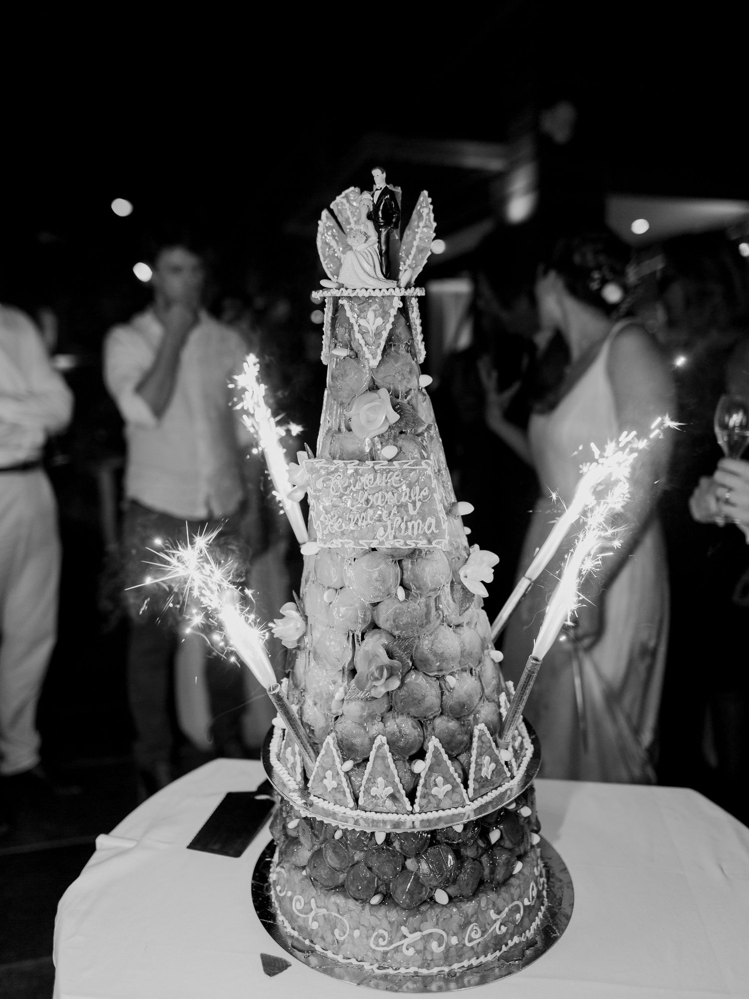 Photo en noir et blanc d'une élégante pièce montée de mariage ornée de cierges magiques et d'une figurine de mariés au sommet à ajaccio
