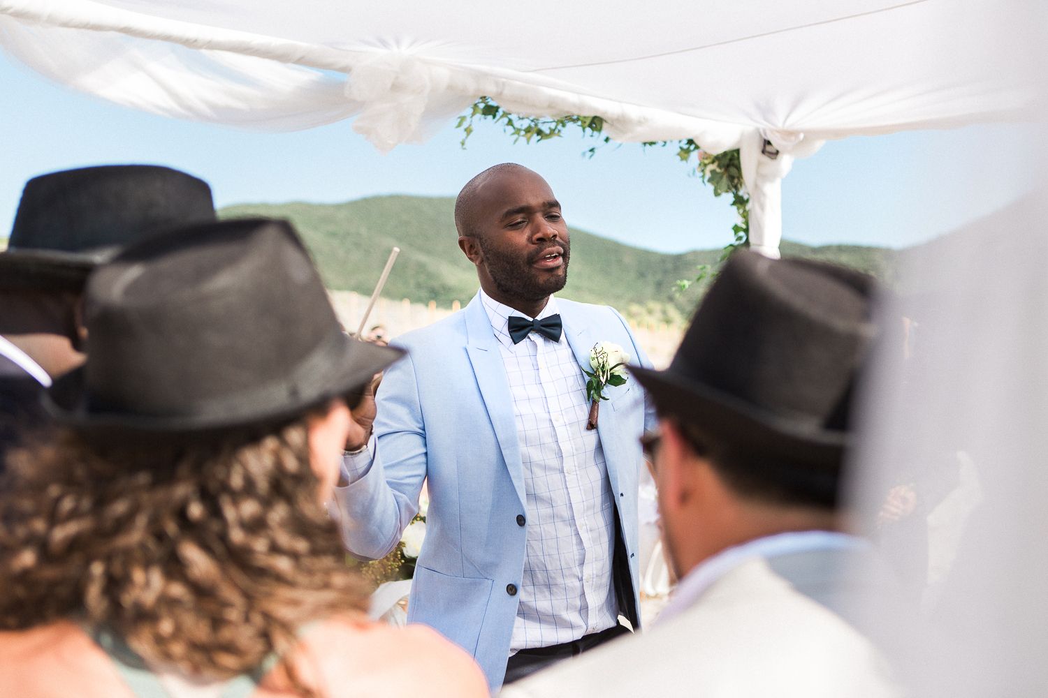 Le marié, vêtu d'un costume bleu clair et d'un nœud papillon, se tient devant l'autel de mariage en plein air, en Corse à Ajaccio