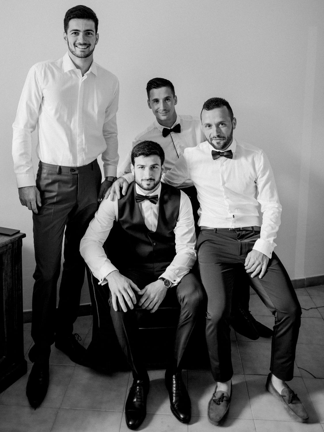 Black and white photo of four well-dressed men in formal attire with bow ties posing together indoors.