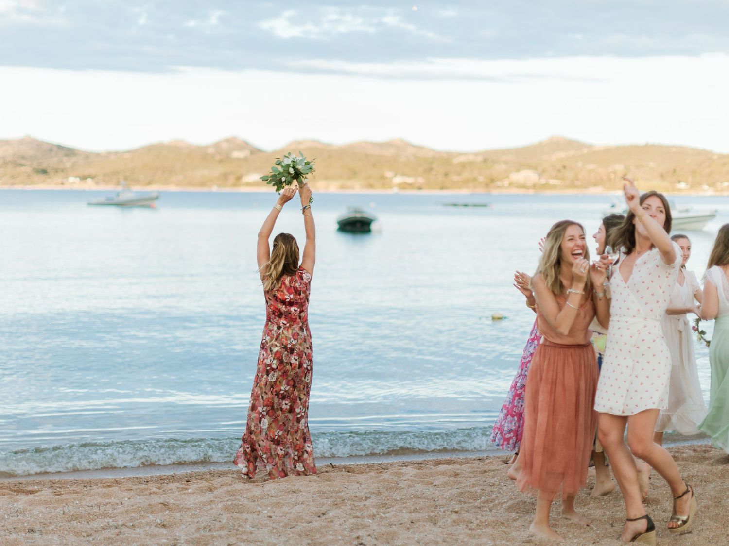 La mariée lance son bouquet à ses demoiselles d'honneur sur une plage de sable fin au coucher du soleil, avec une eau bleue