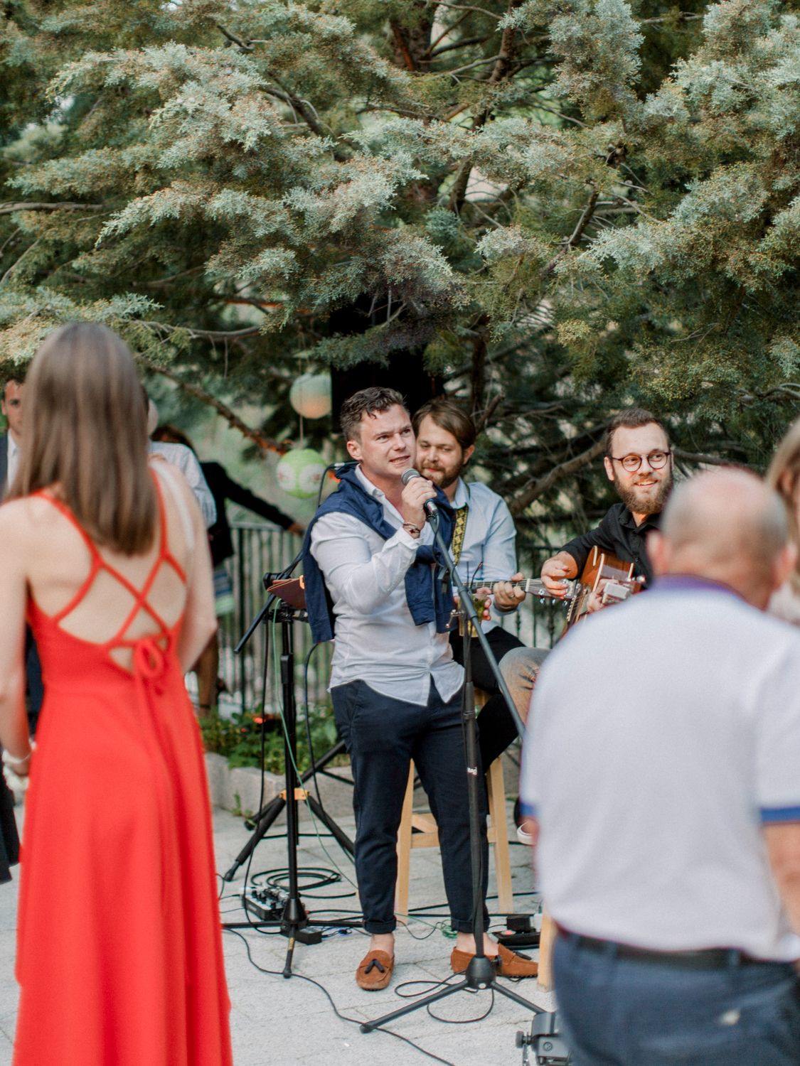 Un groupe de musique joue en plein air lors d'une réception de mariage, les invités en robe rouge regardant le chanteur avec son micro.