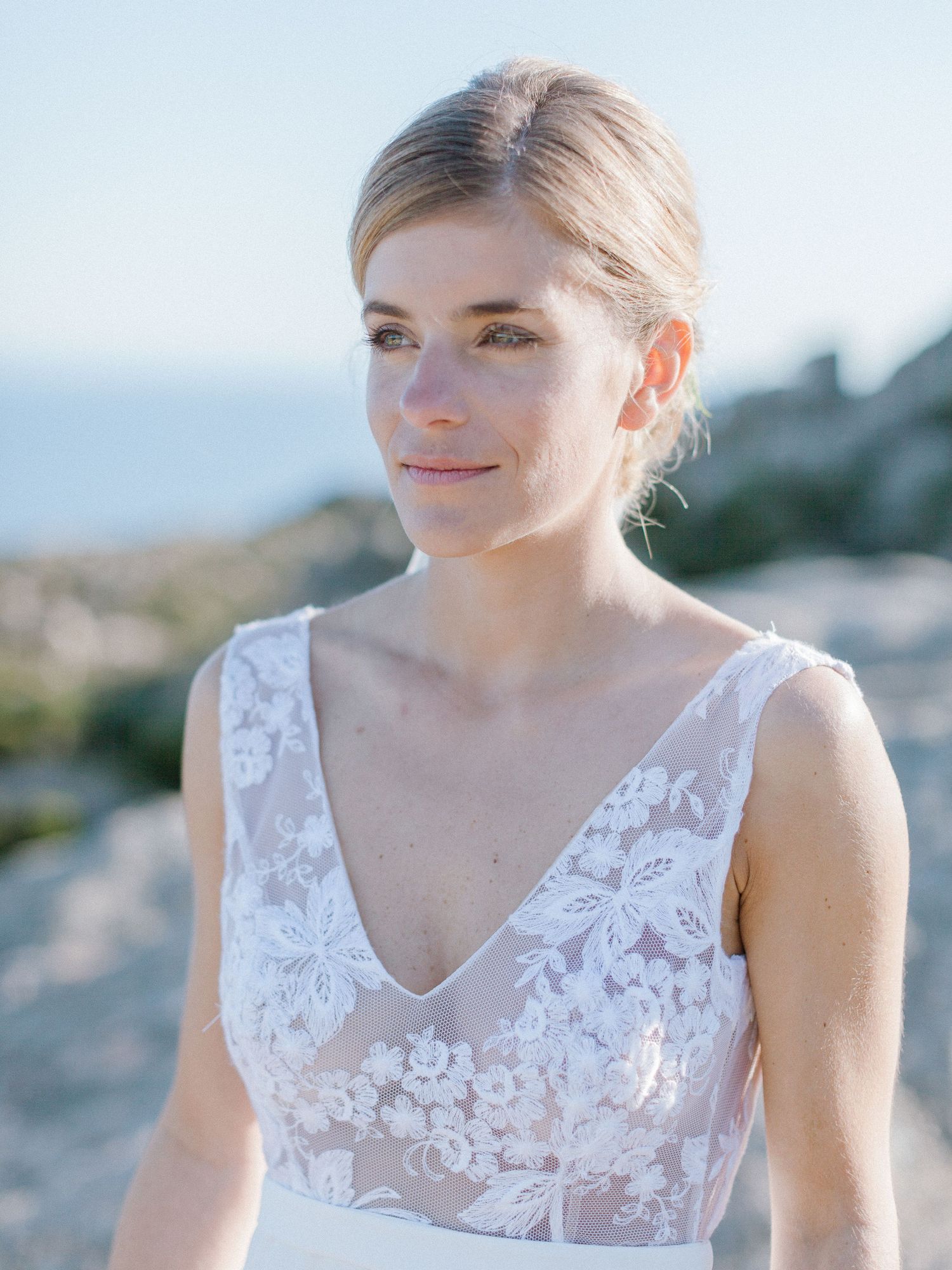 Mariée en robe de mariée en dentelle florale à col en V, coiffure relevée, posant en extérieur à la lumière naturelle.