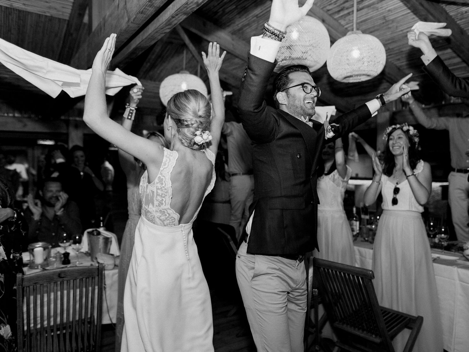 Photo en noir et blanc des mariés dansant joyeusement lors de la réception de mariage, avec les invités en arrière-plan.