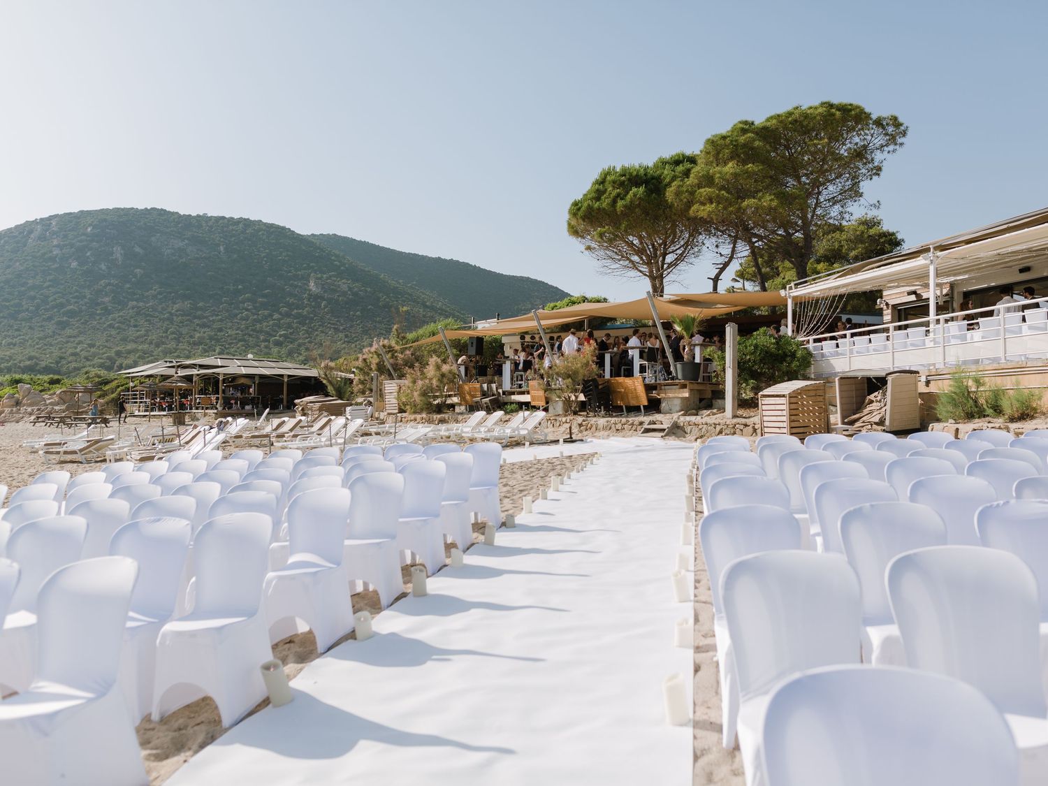 Installation pour un mariage en plein air sur la plage, avec des chaises blanches et une allée, le tout entouré d'une végétation luxuriante