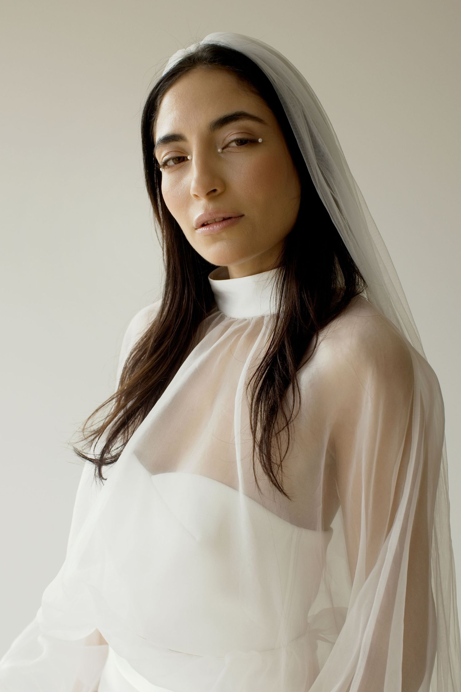 Portrait élégant d'une mariée en robe blanche transparente by romance  à col montant et voile, sur fond neutre.