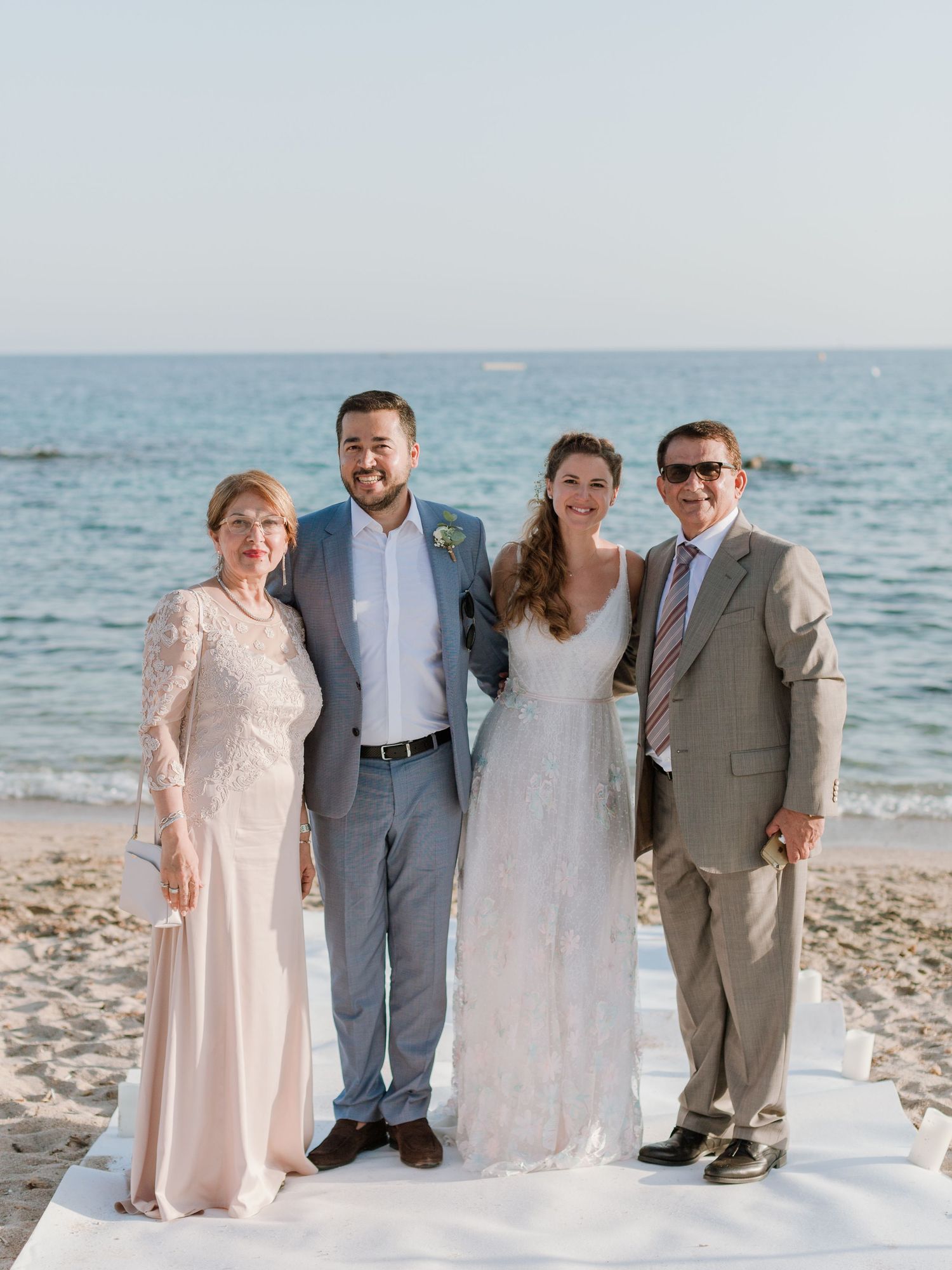 Quatre personnes posent ensemble lors d'une cérémonie de mariage sur la plage, avec l'océan en arrière-plan par une journée ensoleillée.