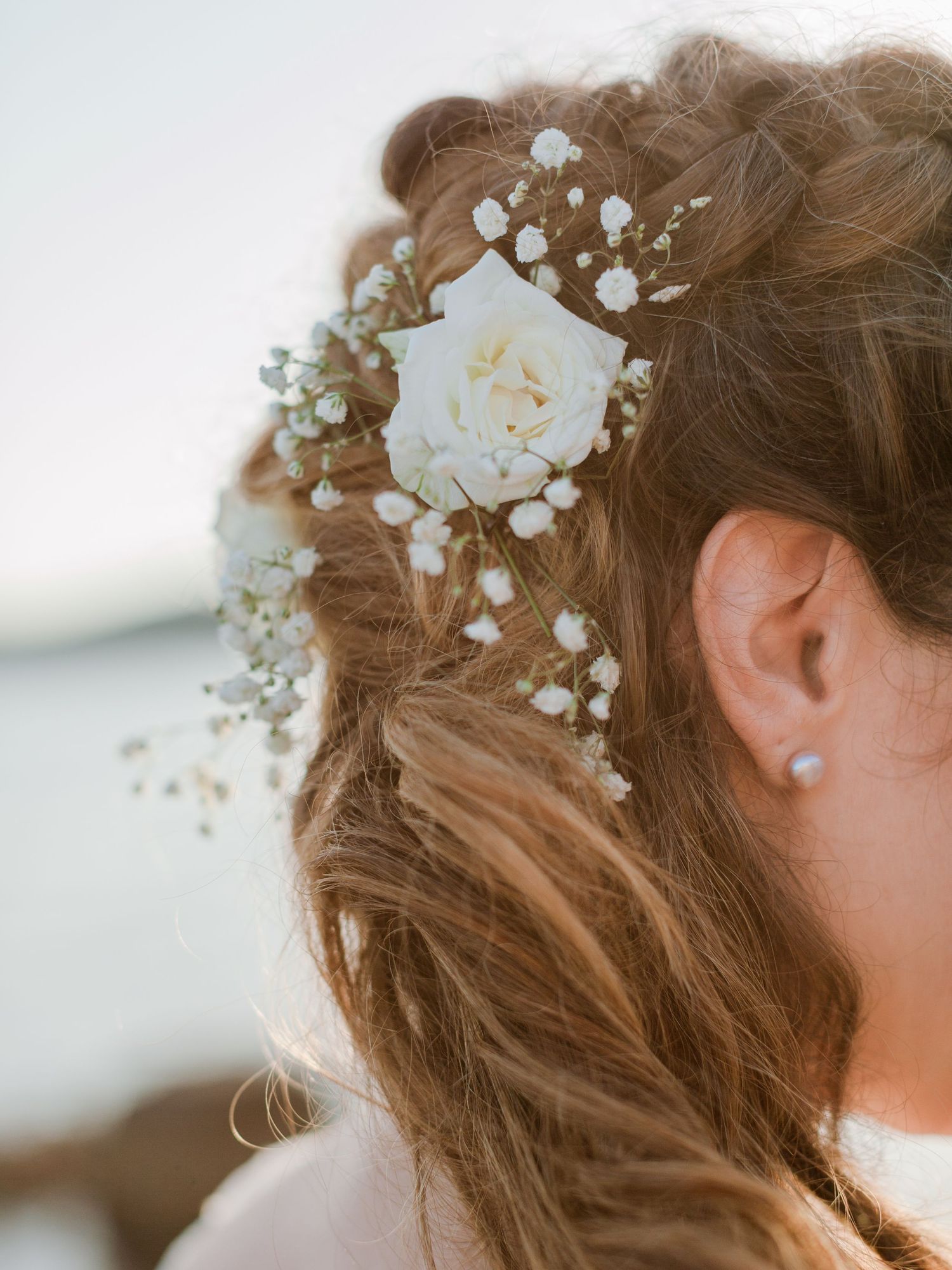 Gros plan sur la coiffure tressée d'une mariée, ornée de roses blanches et de fleurs de gypsophile