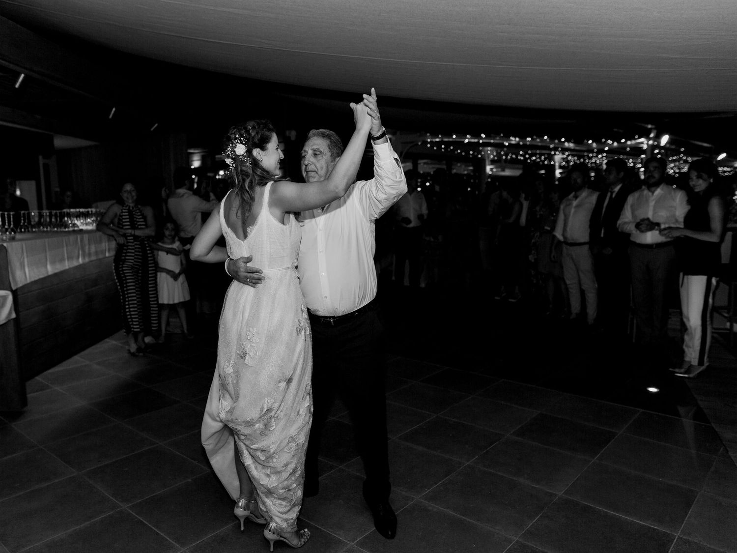 Un couple partageant sa première danse lors d'une réception de mariage, en photographie noir et blanc, avec les invités qui regardent