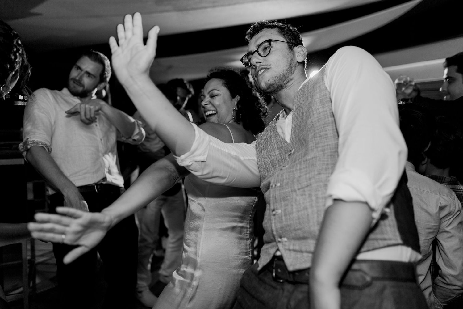 Photo en noir et blanc d'invités dansant et riant joyeusement lors d'une réception de mariage animée.