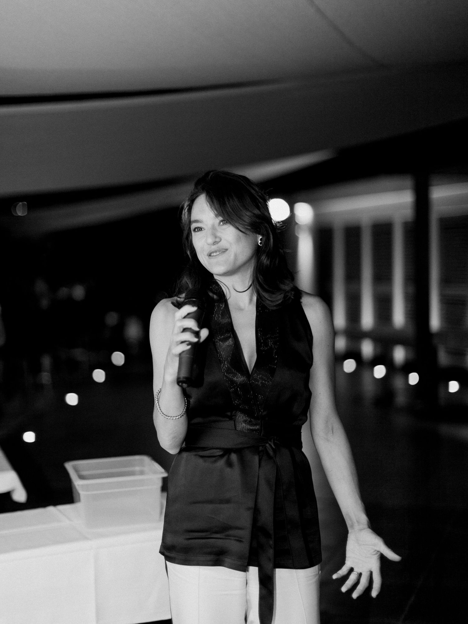 Photo en noir et blanc d'une femme en haut sans manches tenant un microphone lors d'une soirée.