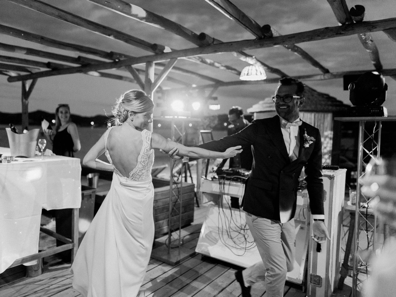 Photo en noir et blanc d'une mariée en robe dos nu dansant avec un homme en costume lors d'une réception de mariage en plein air.