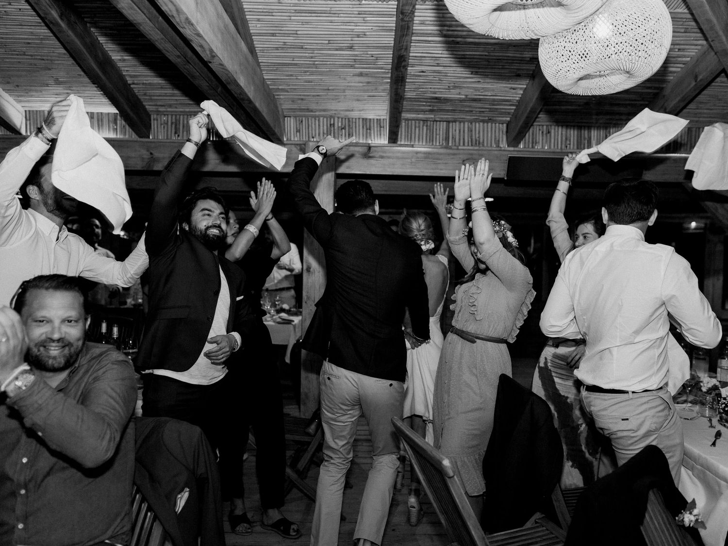Photo en noir et blanc d'invités dansant et faisant la fête lors d'une réception de mariage animée en intérieur.