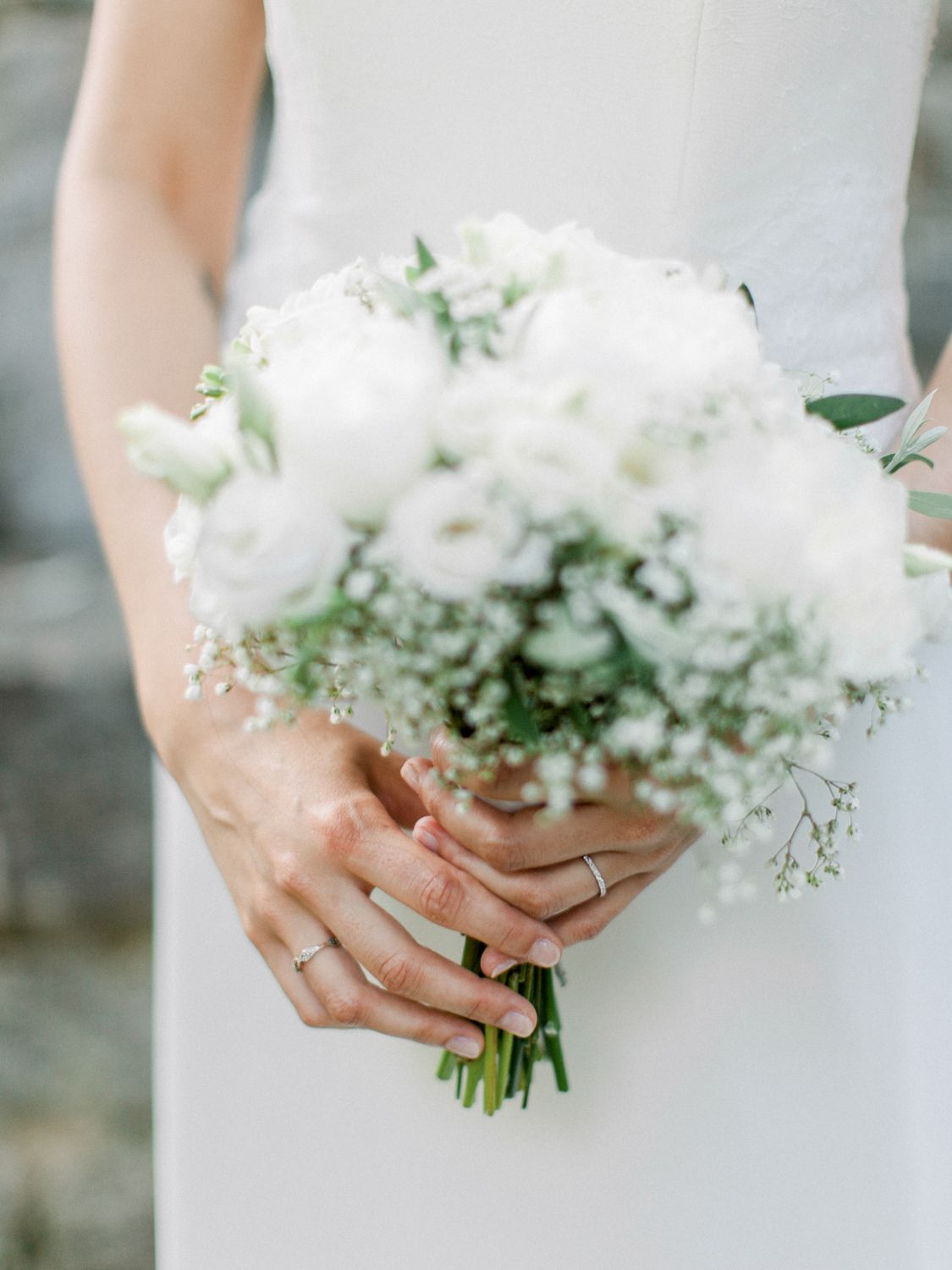 Bride holding a classic white wedding bouquet of roses and baby's breath, wearing a wedding ring on her finger.