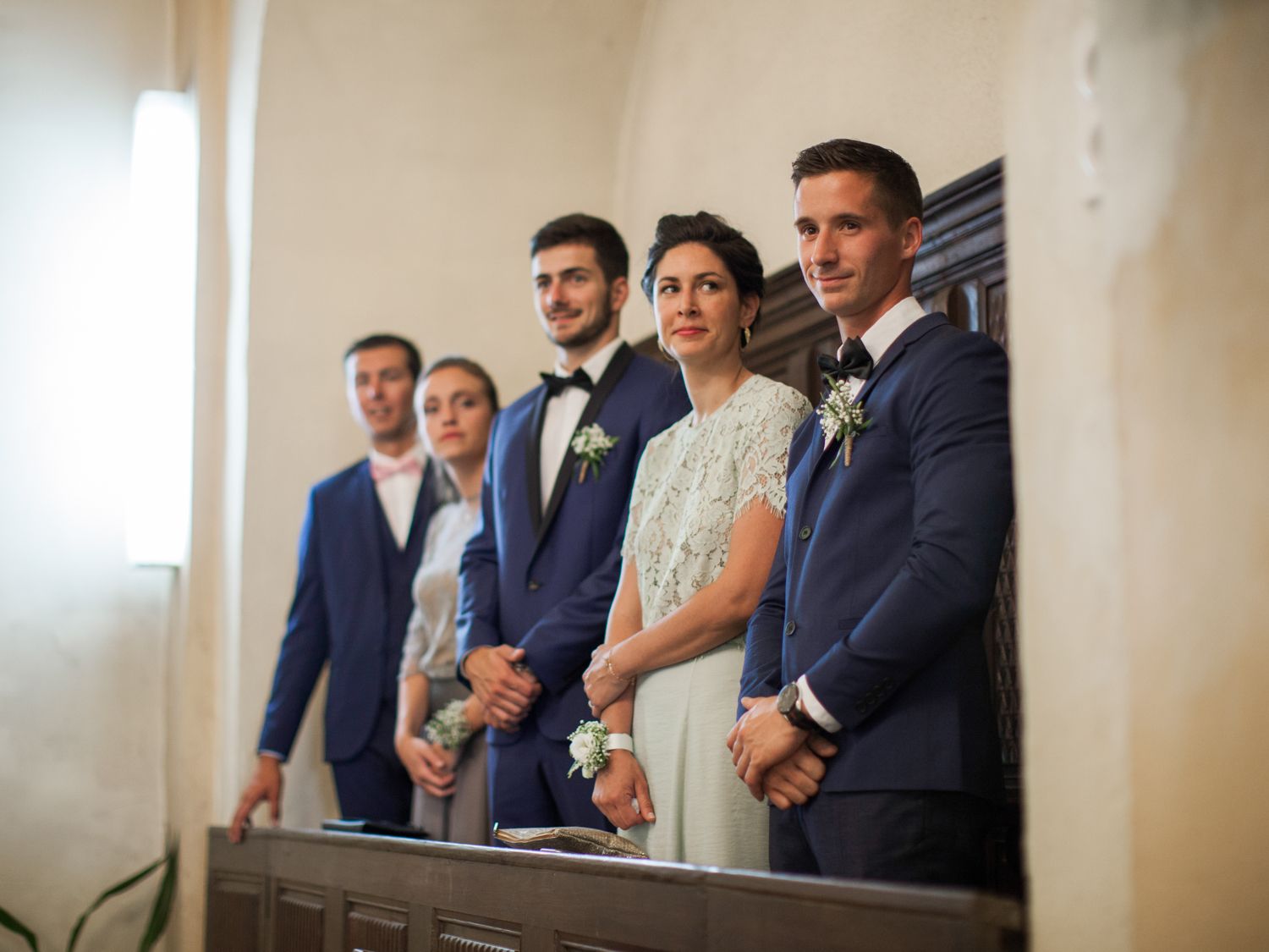 Wedding party in navy suits and white dress posing together inside a elegant venue during a ceremony.