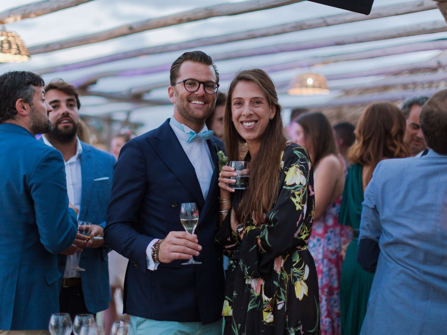 Un couple souriant, coupes de champagne à la main, lors d'une élégante réception de mariage en plein air.