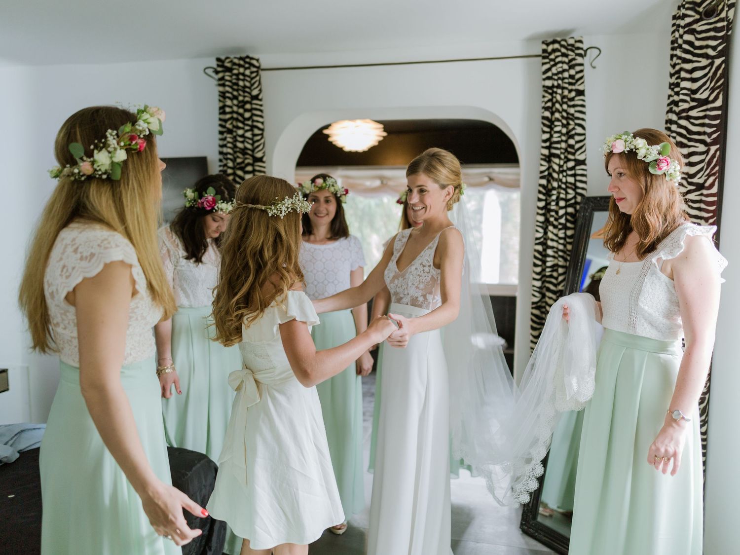 Les demoiselles d'honneur, vêtues de robes vert menthe et coiffées de couronnes de fleurs, aident la mariée à se préparer dans une pièce