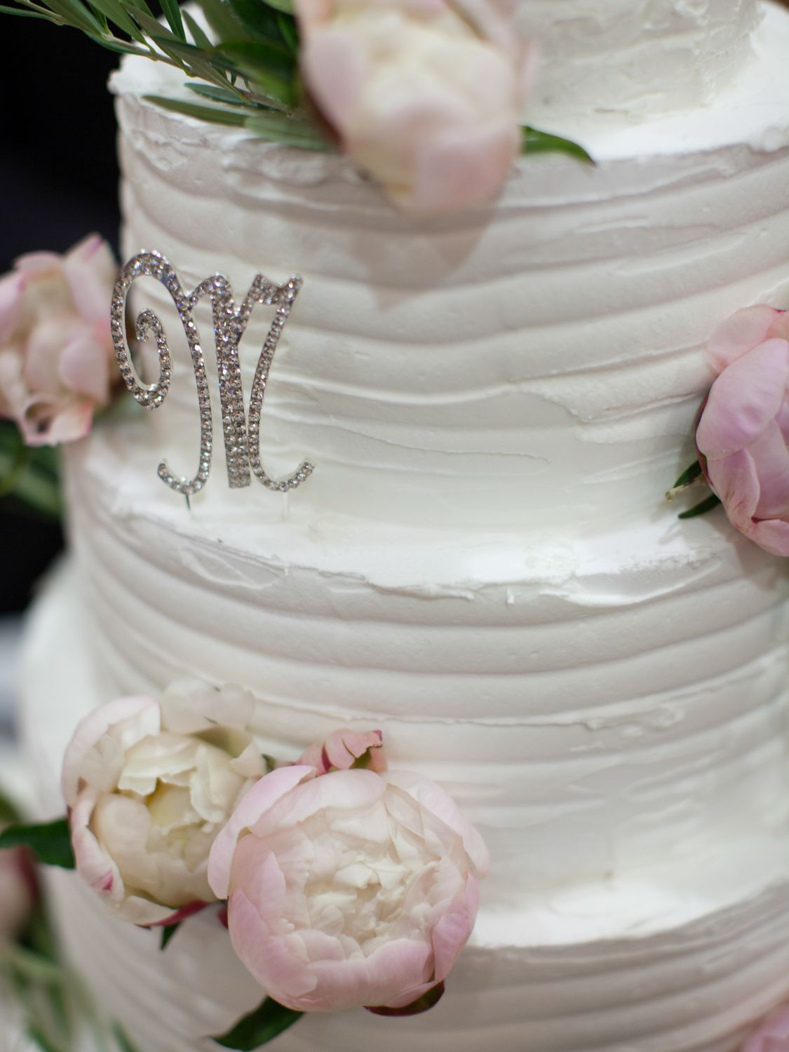 Gâteau de mariage blanc à étages, orné d'un monogramme M en strass et de pivoines roses.
mariage en corse