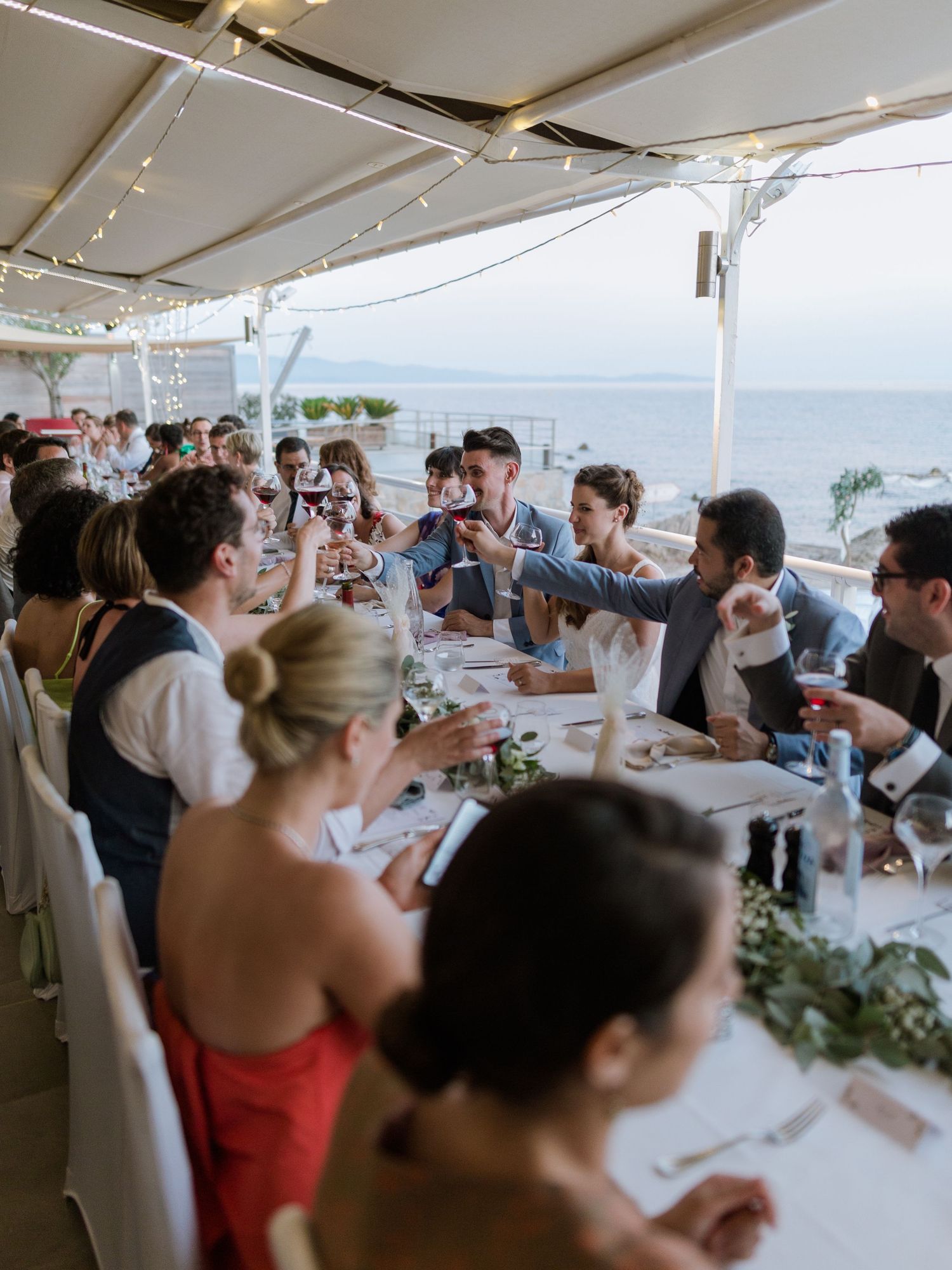 Des invités lèvent leur verre pour porter un toast lors d'une réception de mariage en plein air, au bord de la mer, à l'hotel le week end