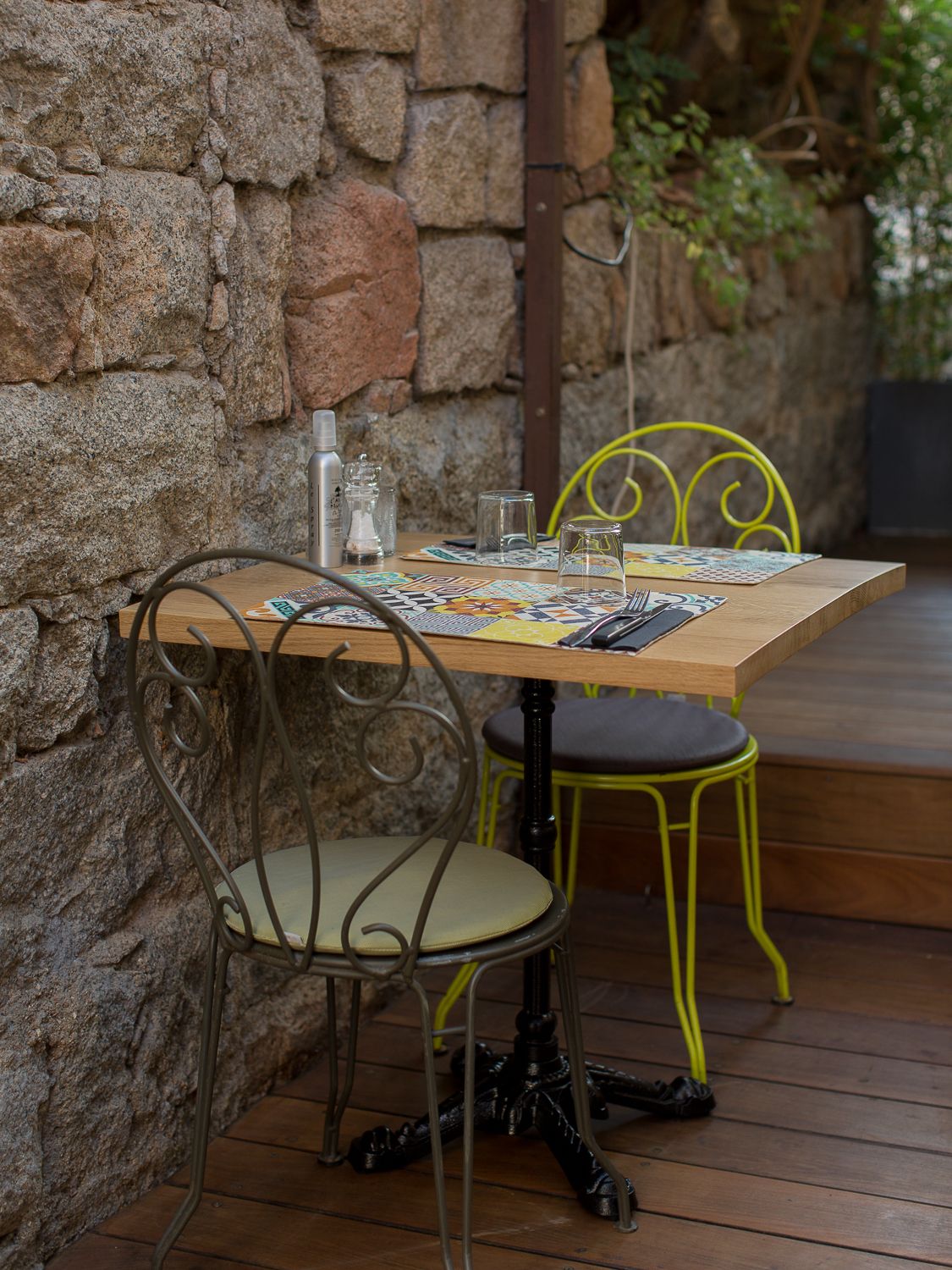 Coin repas cosy avec des chaises en fer jaune et gris autour d'une table en bois, adossée à un mur en pierre. L'orriu Porto-Vecchio.