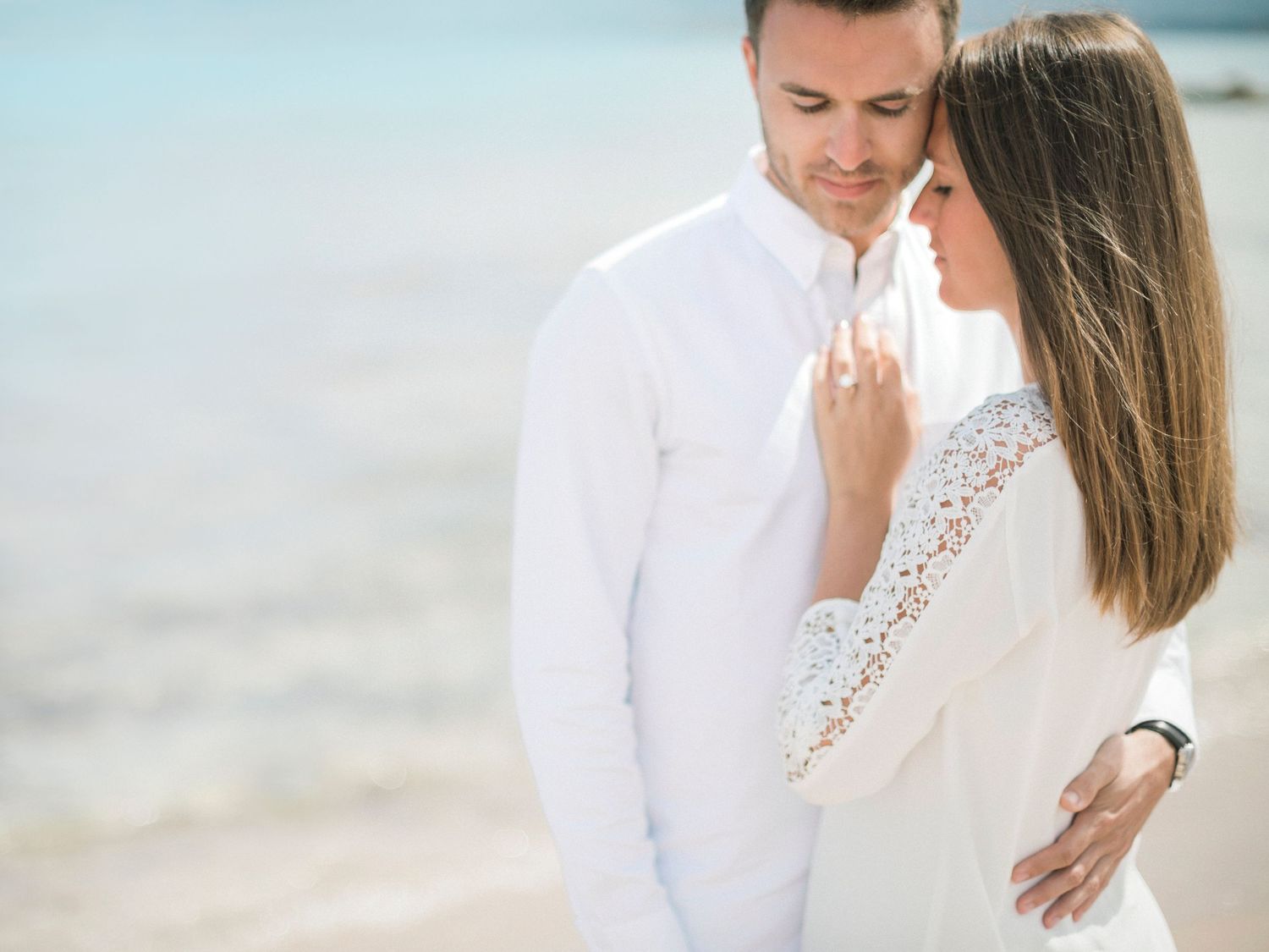 Un couple romantique vêtu de blanc s'enlace sur une plage à Calvi, avec une eau turquoise limpide en arrière-plan.
