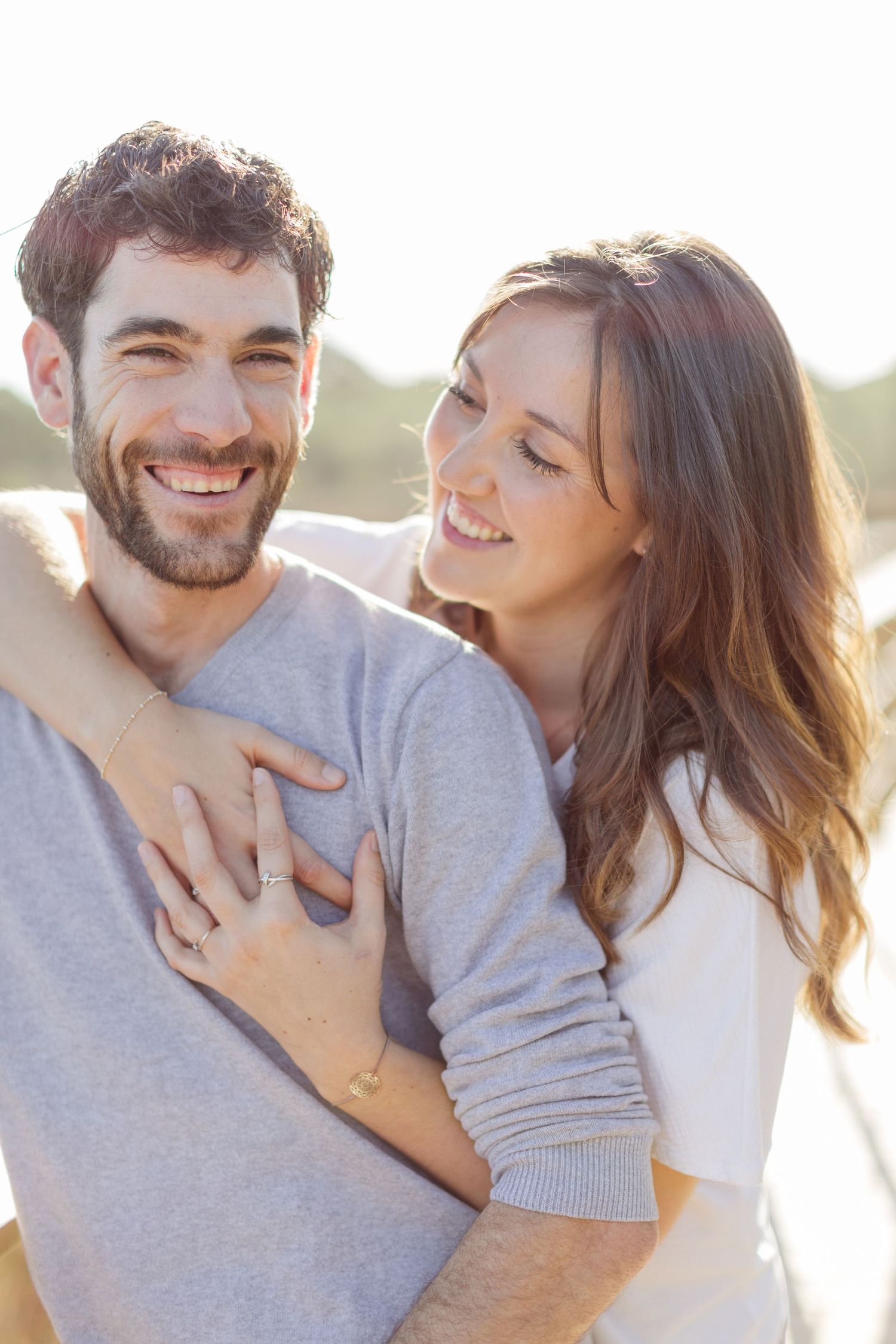 Un couple heureux s'enlace en plein air, la femme souriante serrant l'homme dans ses bras par derrière sous un soleil radieux