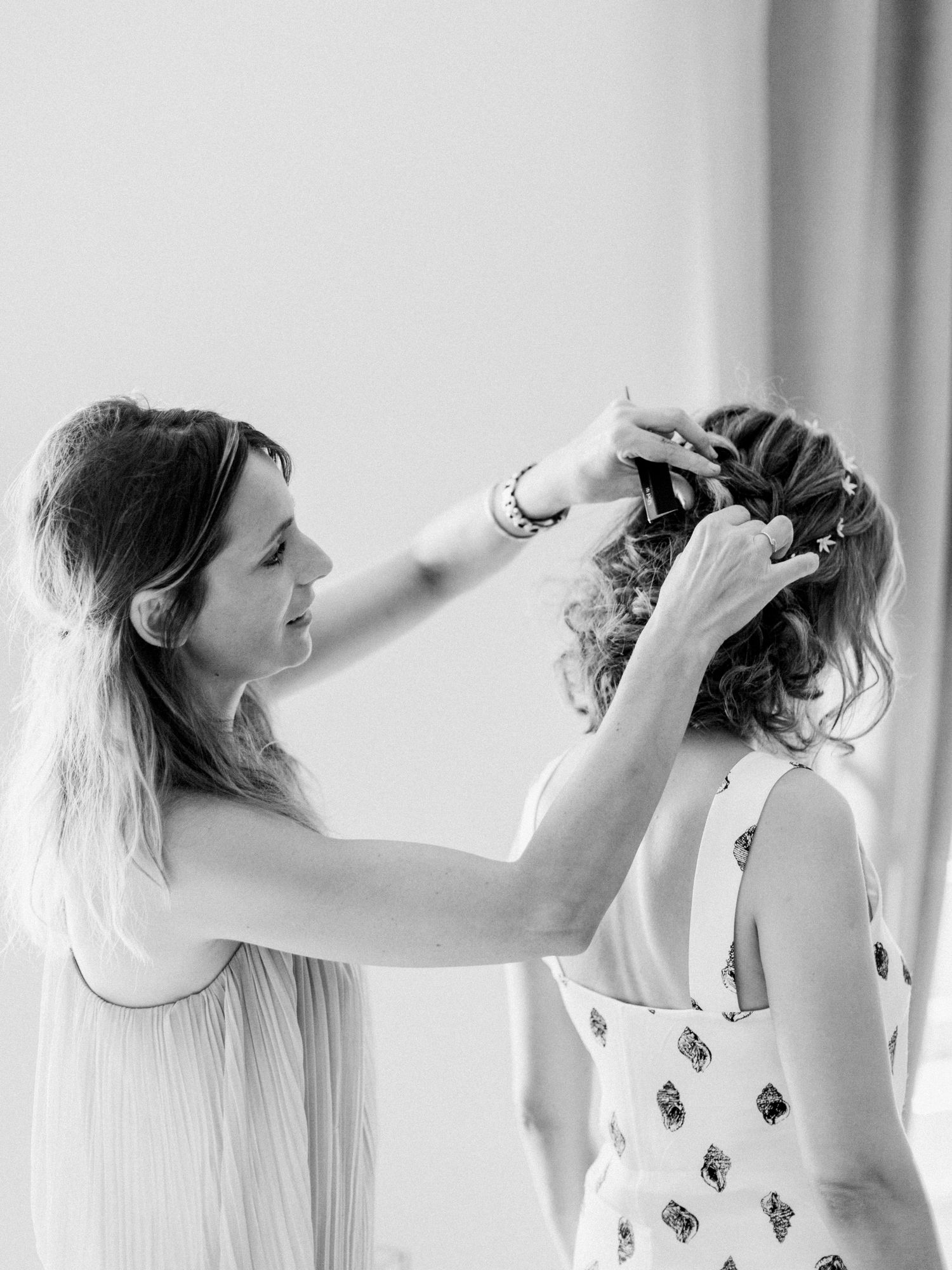 Black and white photo of a woman styling another womans updo hairstyle, perfect for wedding hair inspiration.