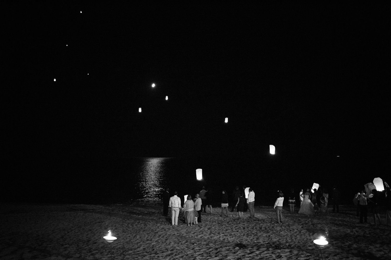 Photo en noir et blanc de personnes lâchant des lanternes célestes sur une plage la nuit, les lumières scintillantes à Ajaccio
