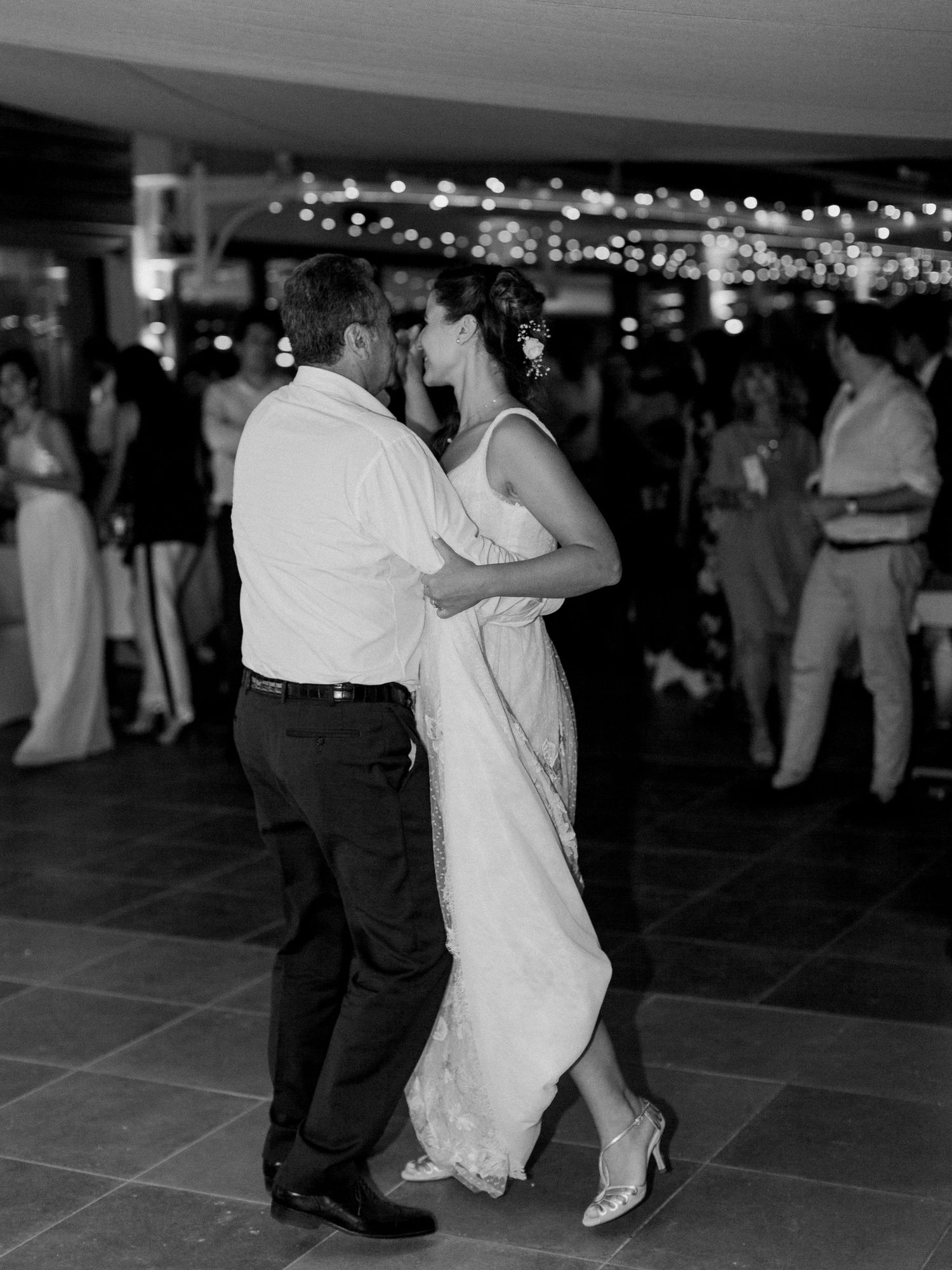 Photo en noir et blanc d'une mariée et d'un marié partageant leur première danse lors d'une réception de mariage, avec des invités