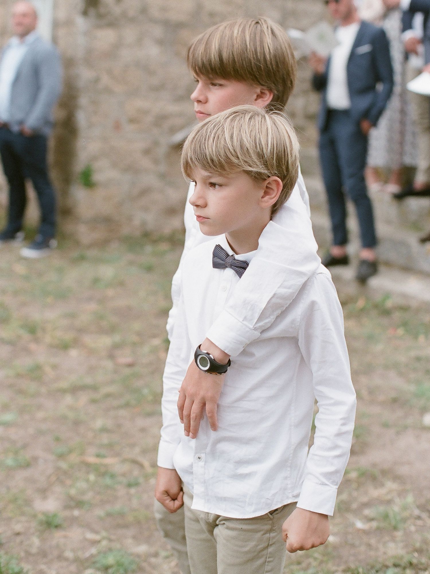 Deux jeunes garçons en chemises blanches et nœuds papillon lors d'une cérémonie de mariage en plein air.