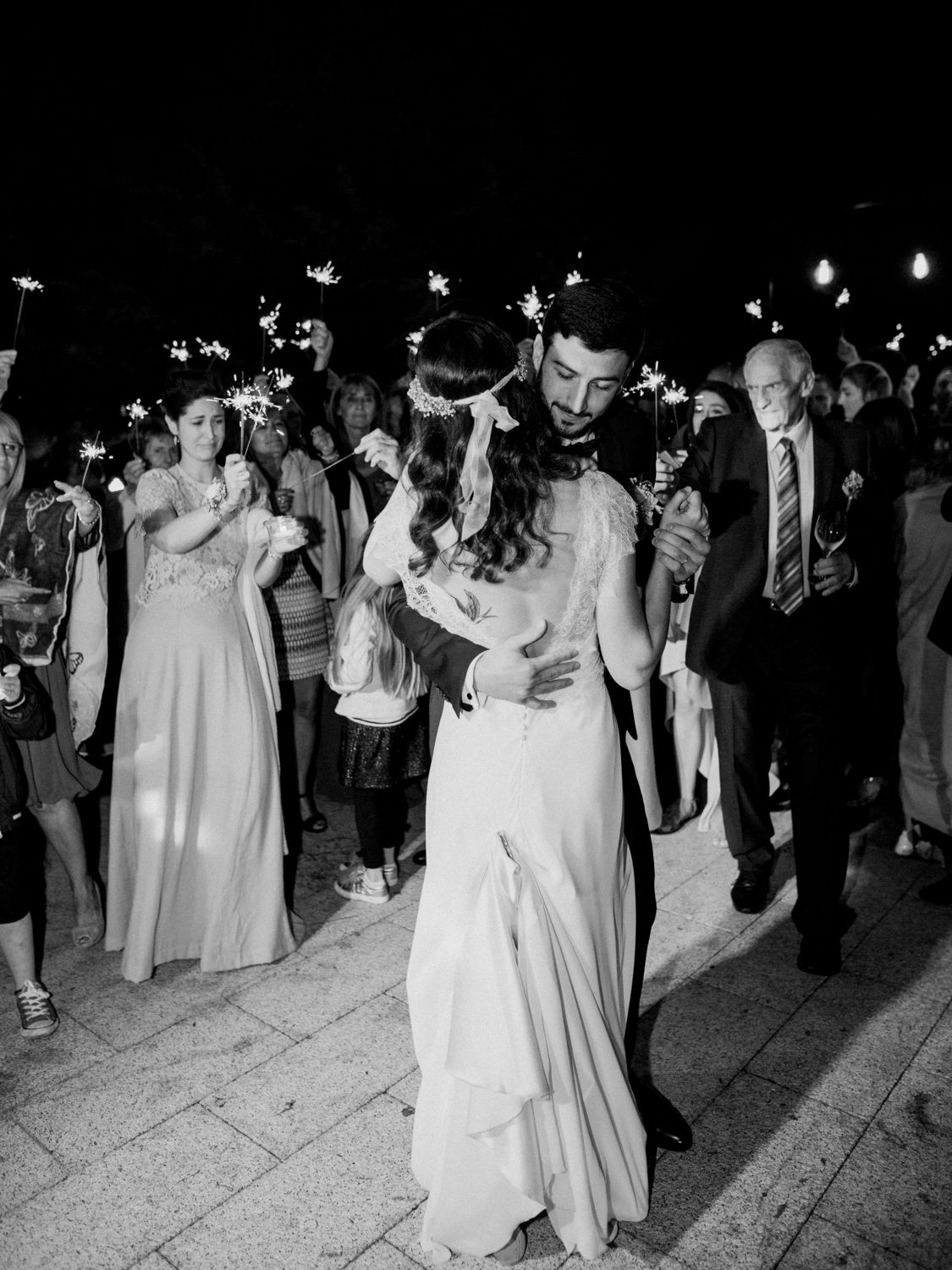 Photo en noir et blanc de jeunes mariés s'embrassant lors d'une sortie sous une pluie d'étincelles à leur réception de mariage.