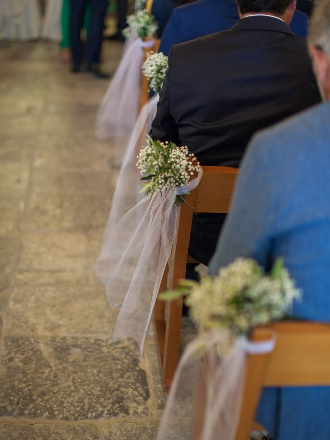 Wedding ceremony aisle chairs decorated with baby's breath flowers and tulle ribbon bows in a church.