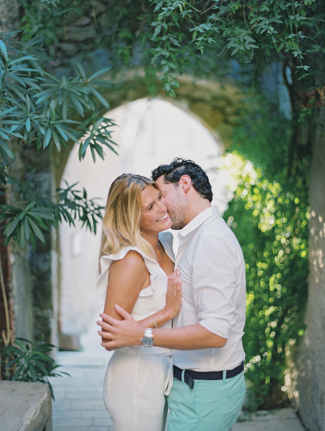 Un couple romantique s'enlaçant sous une arche de pierre entourée d'une végétation luxuriante, en Provence